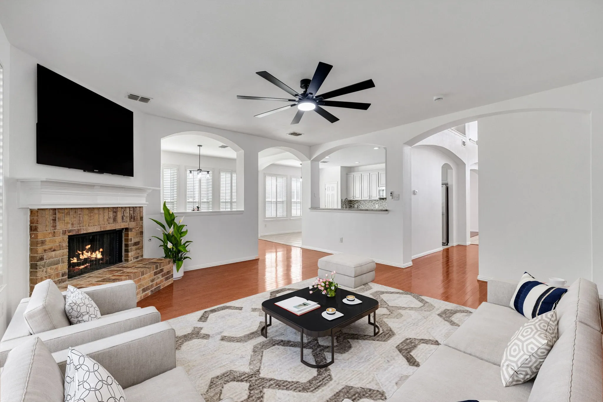 Brick fireplace with a substantial hearth, wood-finish flooring, recessed lighting, and arched architectural openings