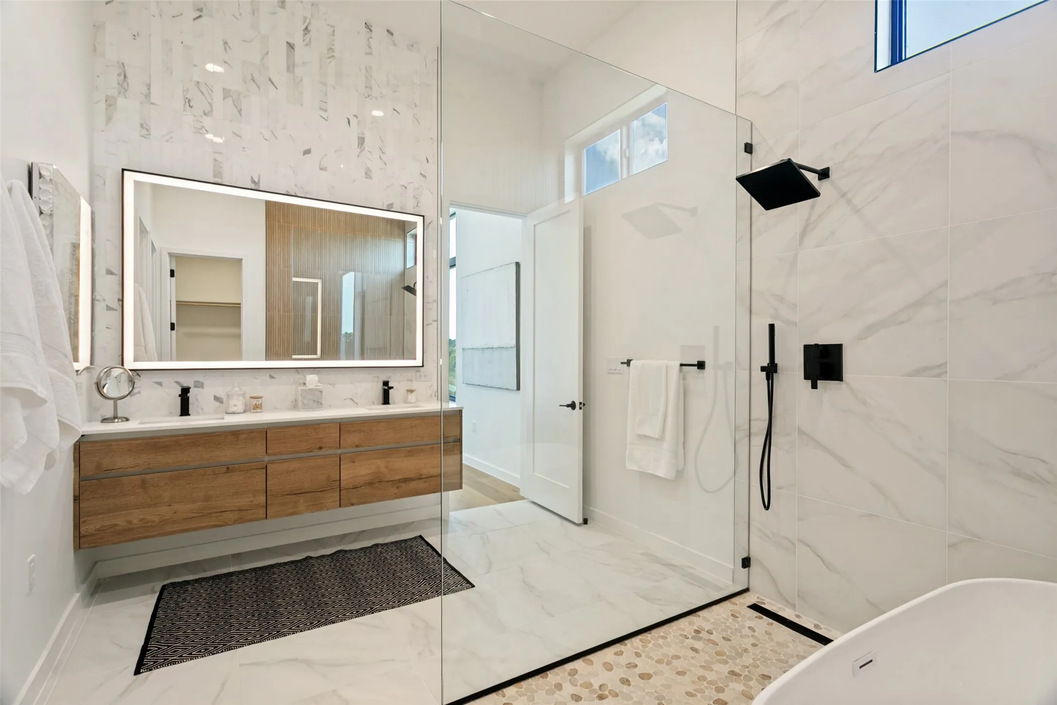 Floating wood-finish double vanity with dual sinks and under cabinet floor lighting, illuminated mirror, natural light.