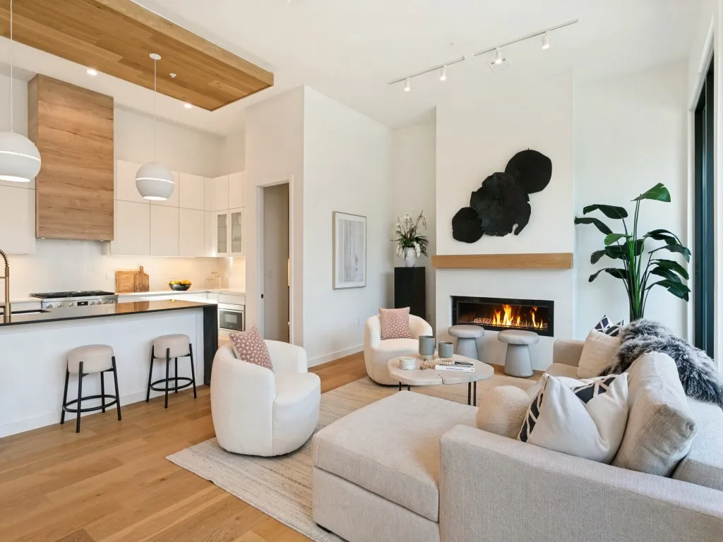 Open-concept space featuring white oak wood floor, a kitchen with flat-panel cabinetry and oak wood-paneled range hood, a linear gas fireplace, and a walk in pantry or bar area.