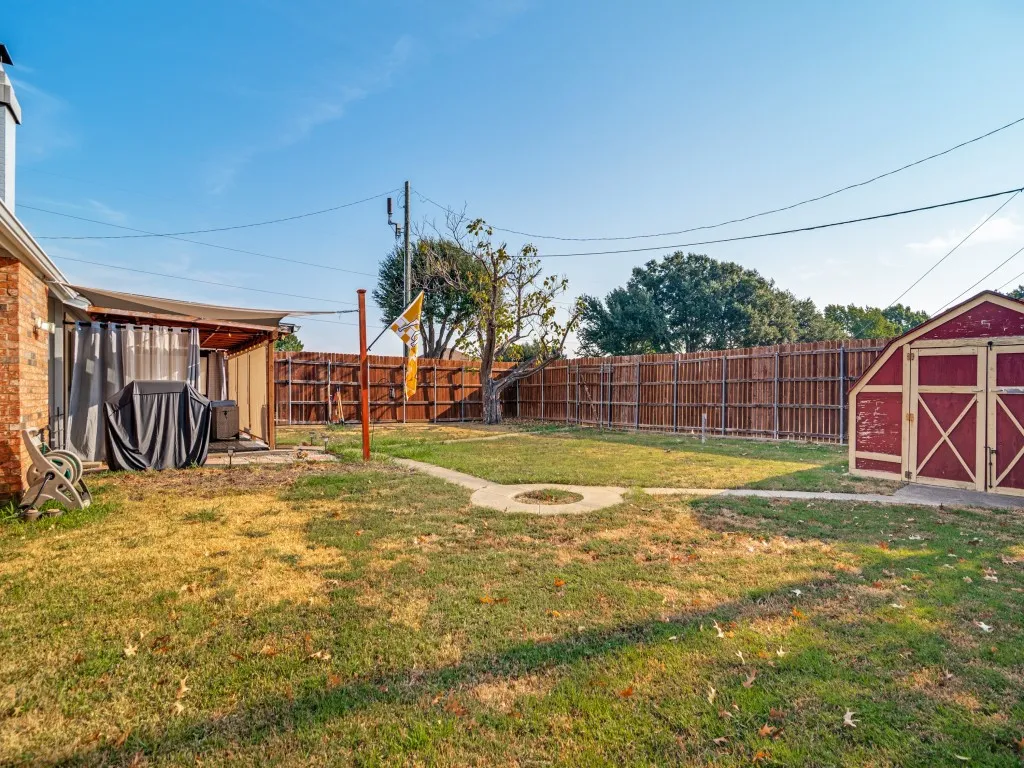 Expansive outdoor space featuring a covered patio, a detached storage shed, privacy fencing, and a concrete pathway