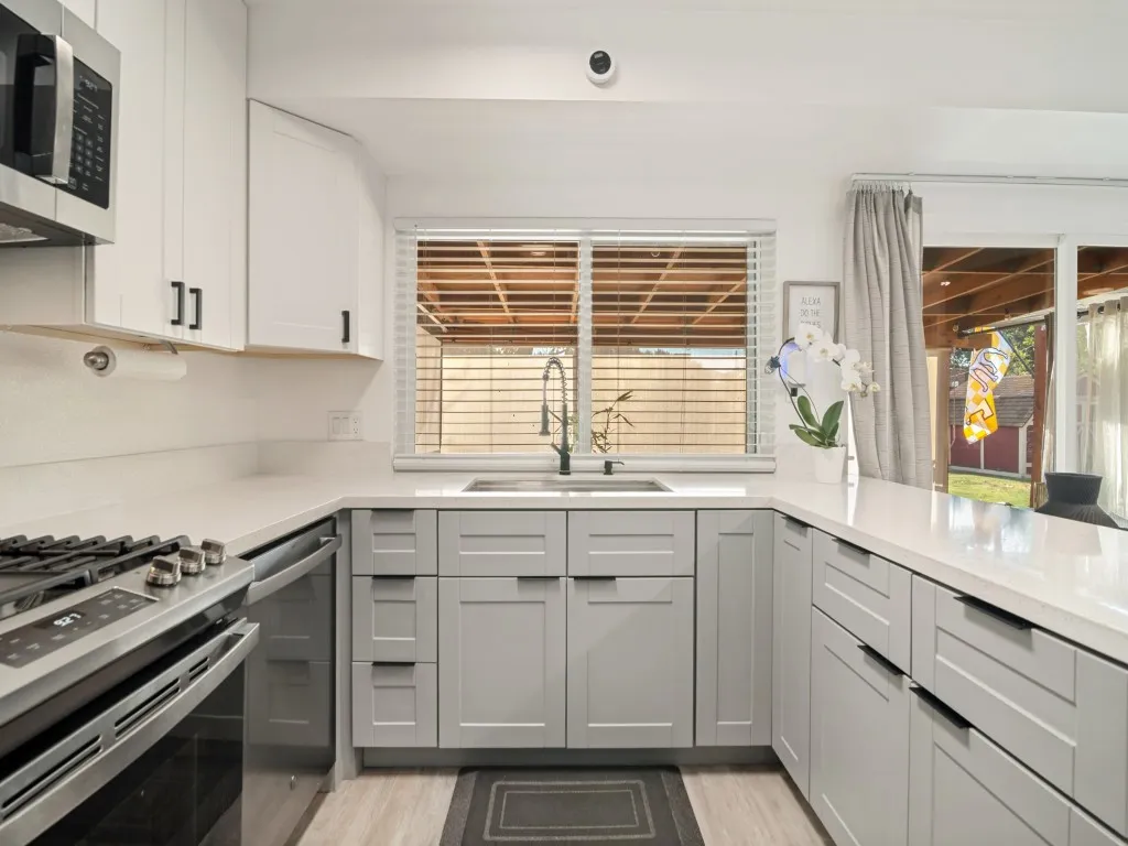 U-shaped kitchen featuring light gray and white shaker cabinetry, light-toned countertops, stainless steel appliances, and wood-finish flooring
