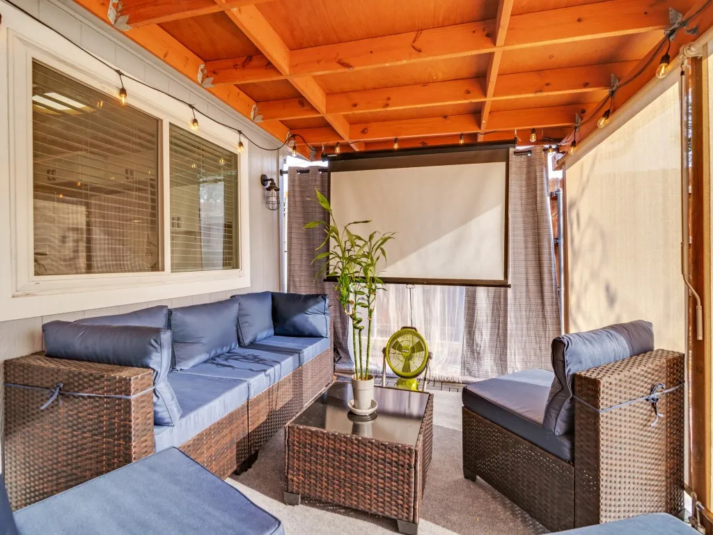Covered patio with an exposed wood beam ceiling, string lighting, and a mounted projector screen