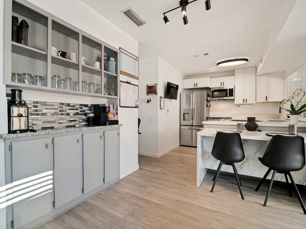 Wood-finish flooring, white cabinetry with black hardware, stainless steel appliances, breakfast bar with waterfall edge, and track lighting