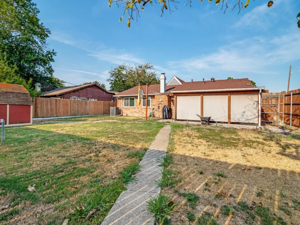 Expansive backyard featuring a red storage shed with a shingled roof, a concrete pathway, and a privacy fence