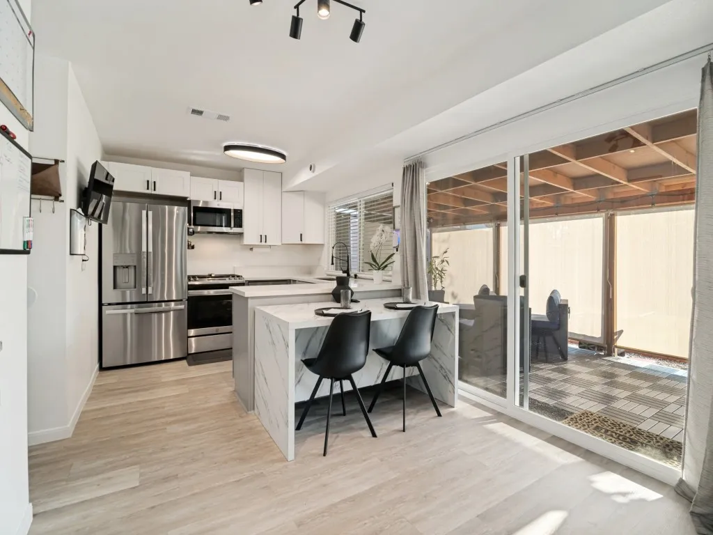Modern kitchen featuring white cabinetry, stainless steel appliances, a center island with seating, wood-finish flooring, and a large sliding glass door