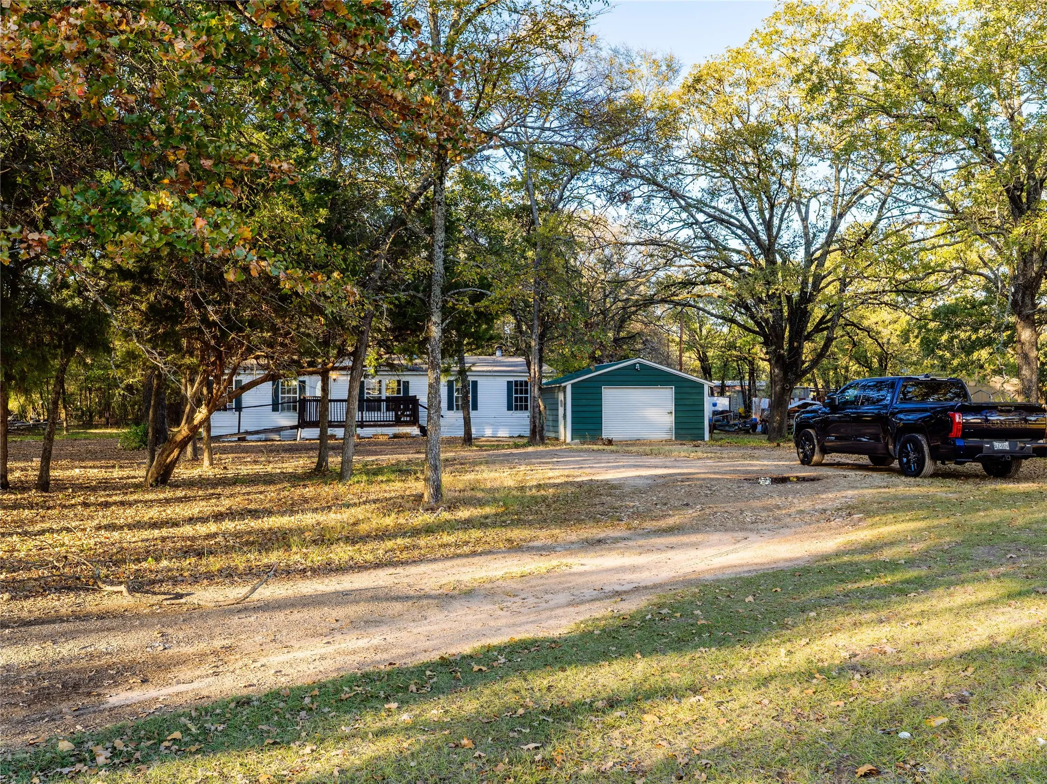 Expansive lot with mature trees, a white-sided residence, a covered porch, and a detached green storage structure