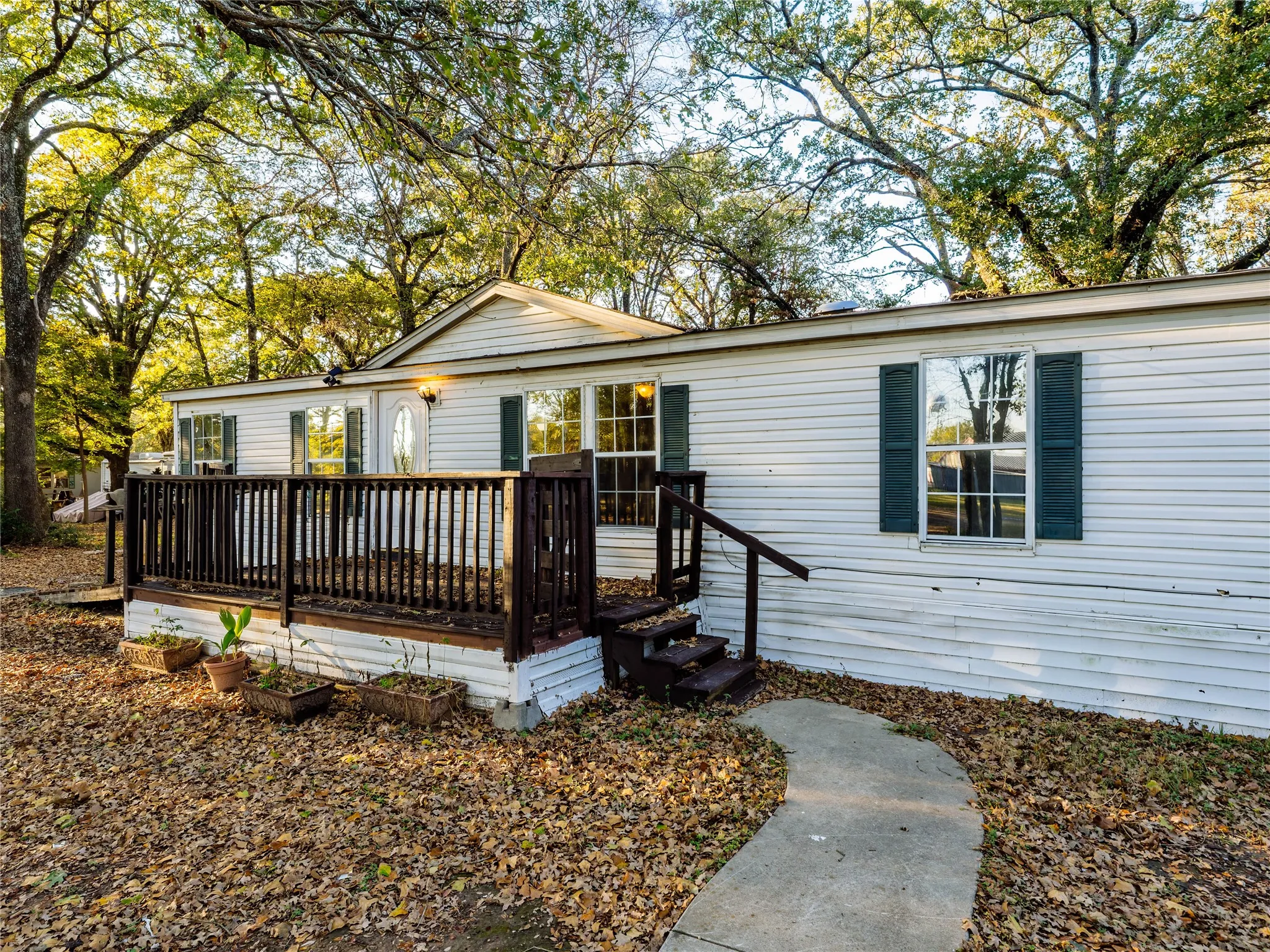 White siding exterior with a wood deck, dark wood railings, and a concrete pathway