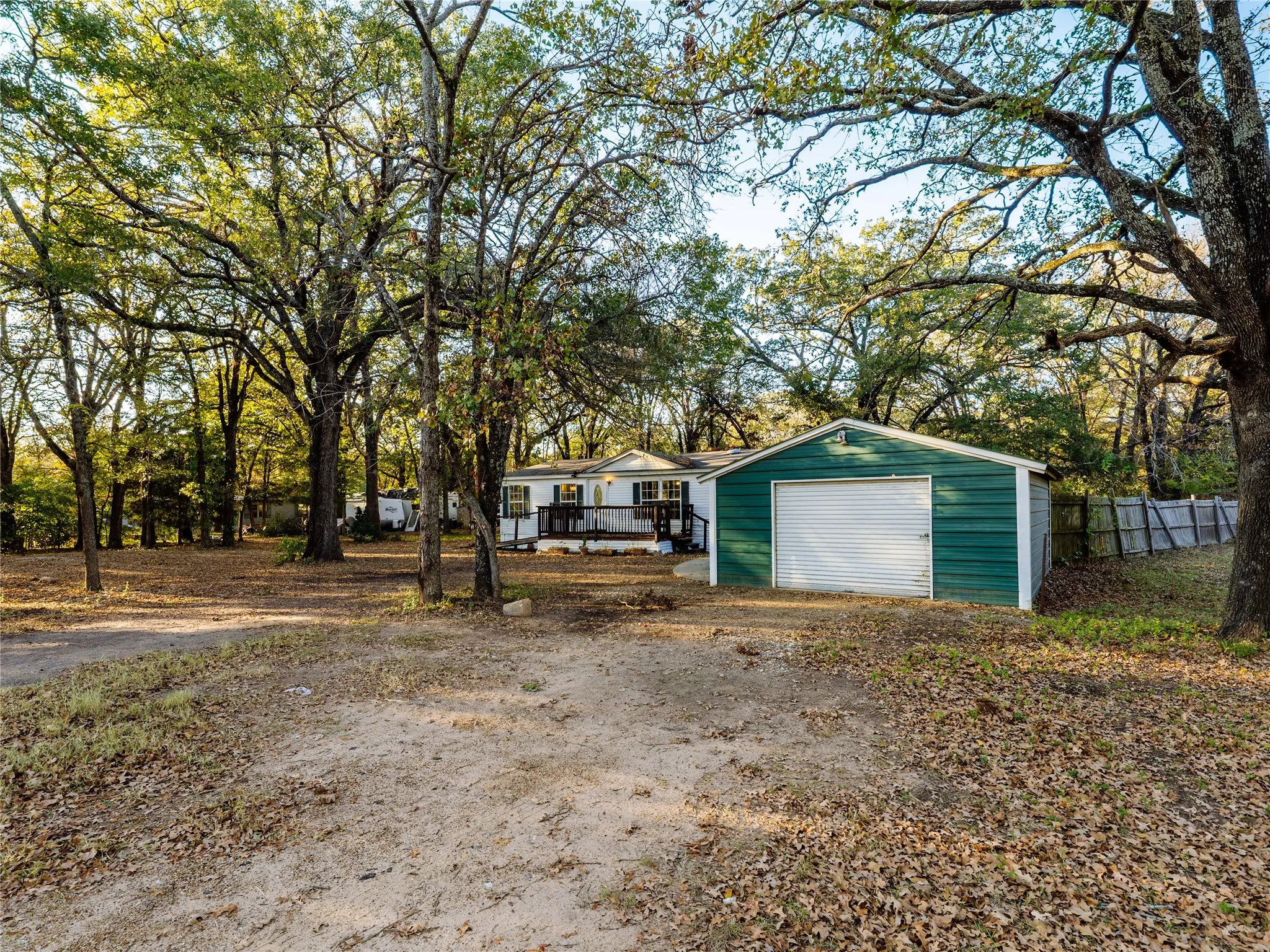 Detached garage with white roll-up door, expansive treed lot, and a residential structure with a covered porch