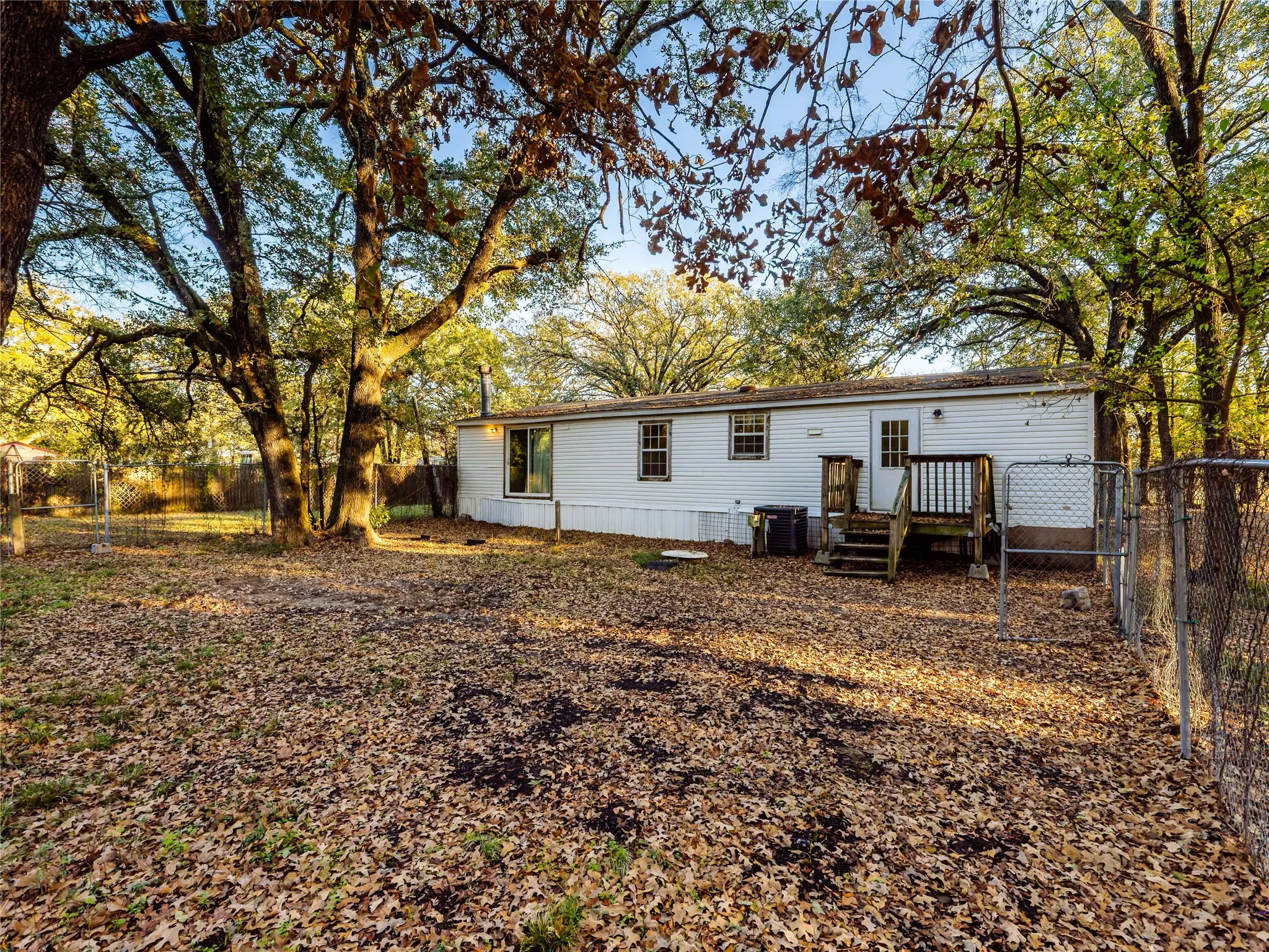 Expansive yard featuring mature trees, white siding, a wooden deck, and a chain-link fence