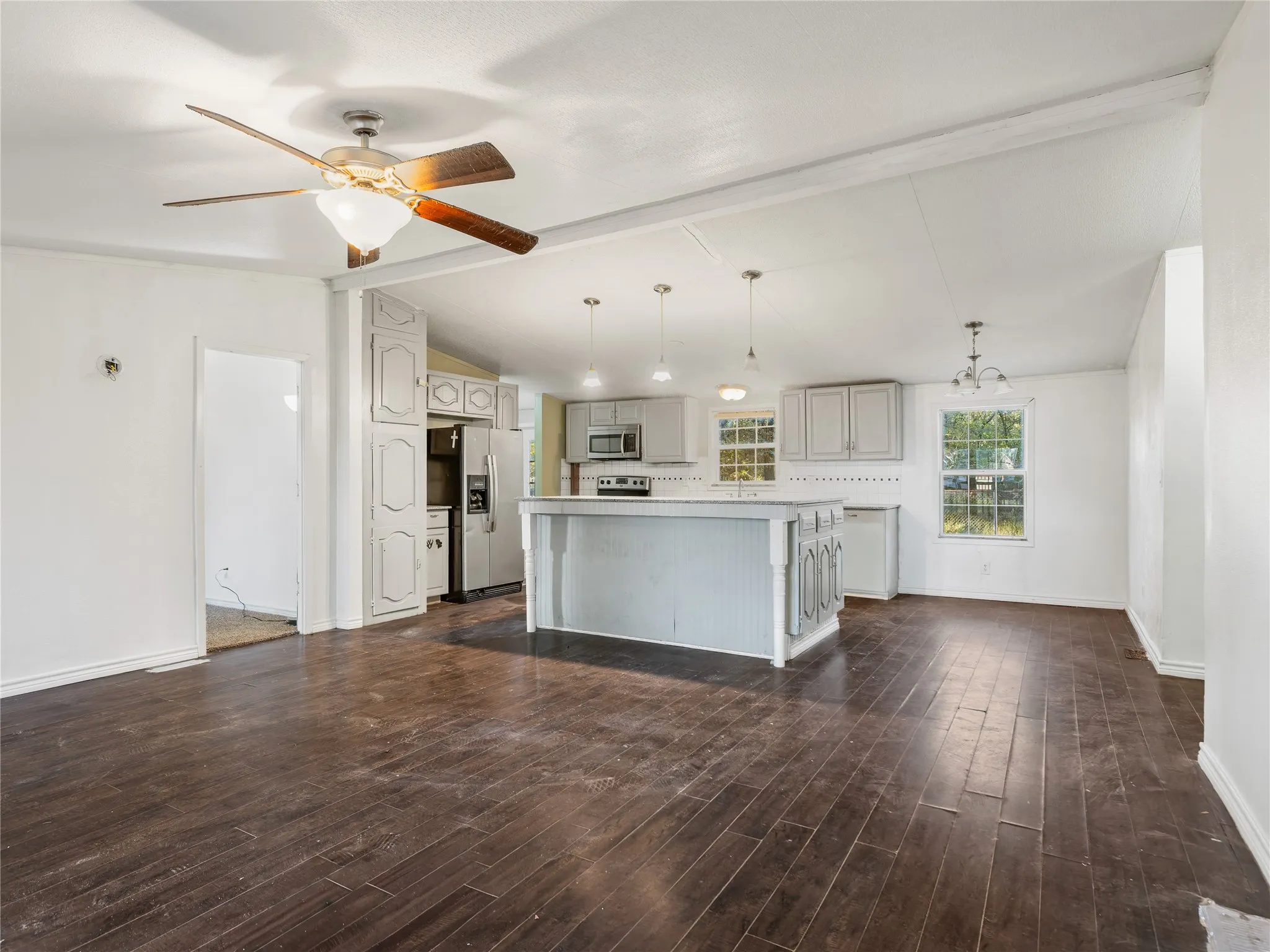 Vaulted ceiling with exposed beams, ceiling fan, wood-finish flooring, white cabinetry, and a kitchen island with pendant lighting