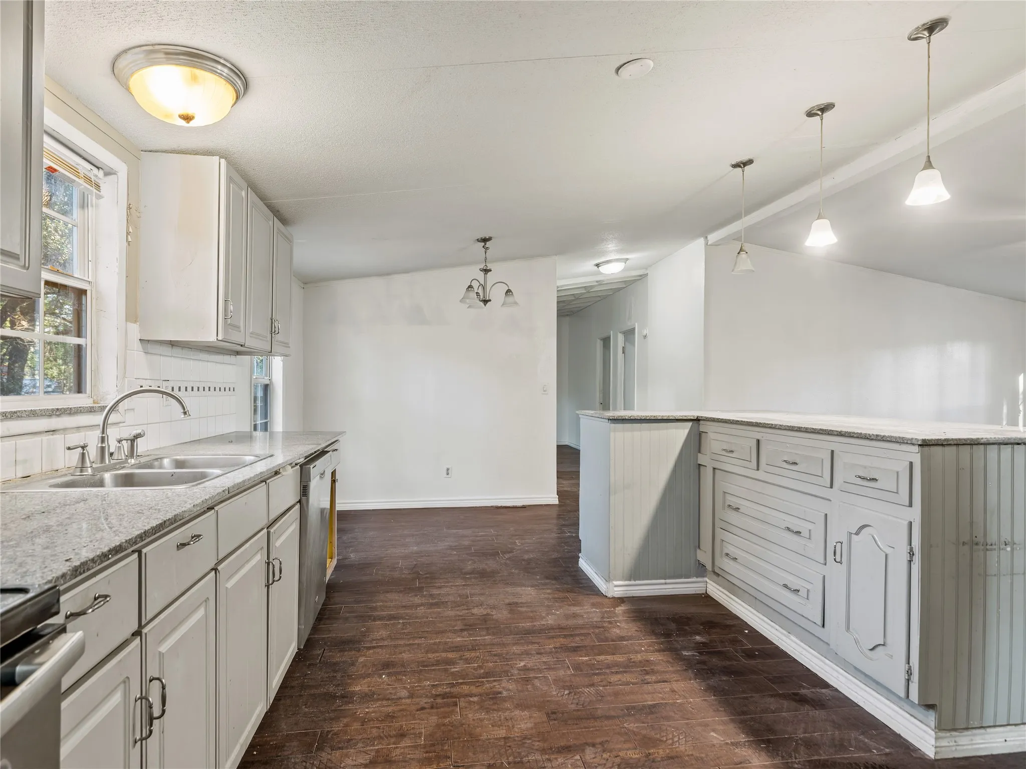 Kitchen featuring light-toned cabinetry, dual basin stainless steel sink, granite-style countertops, pendant lighting, and wood-finish flooring