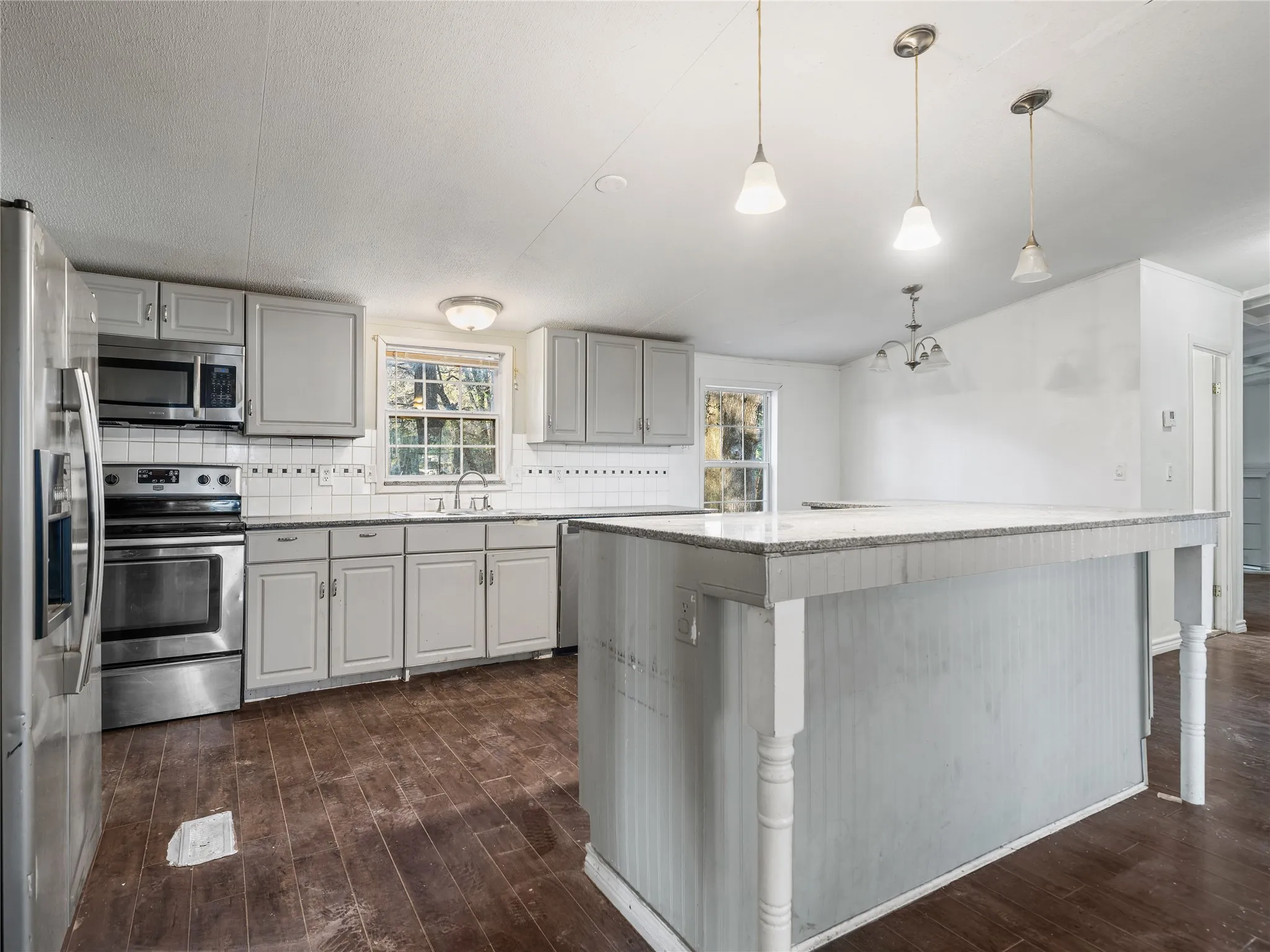 Kitchen featuring light gray cabinetry, stainless steel appliances, white tile backsplash, and an island with a light-colored countertop
