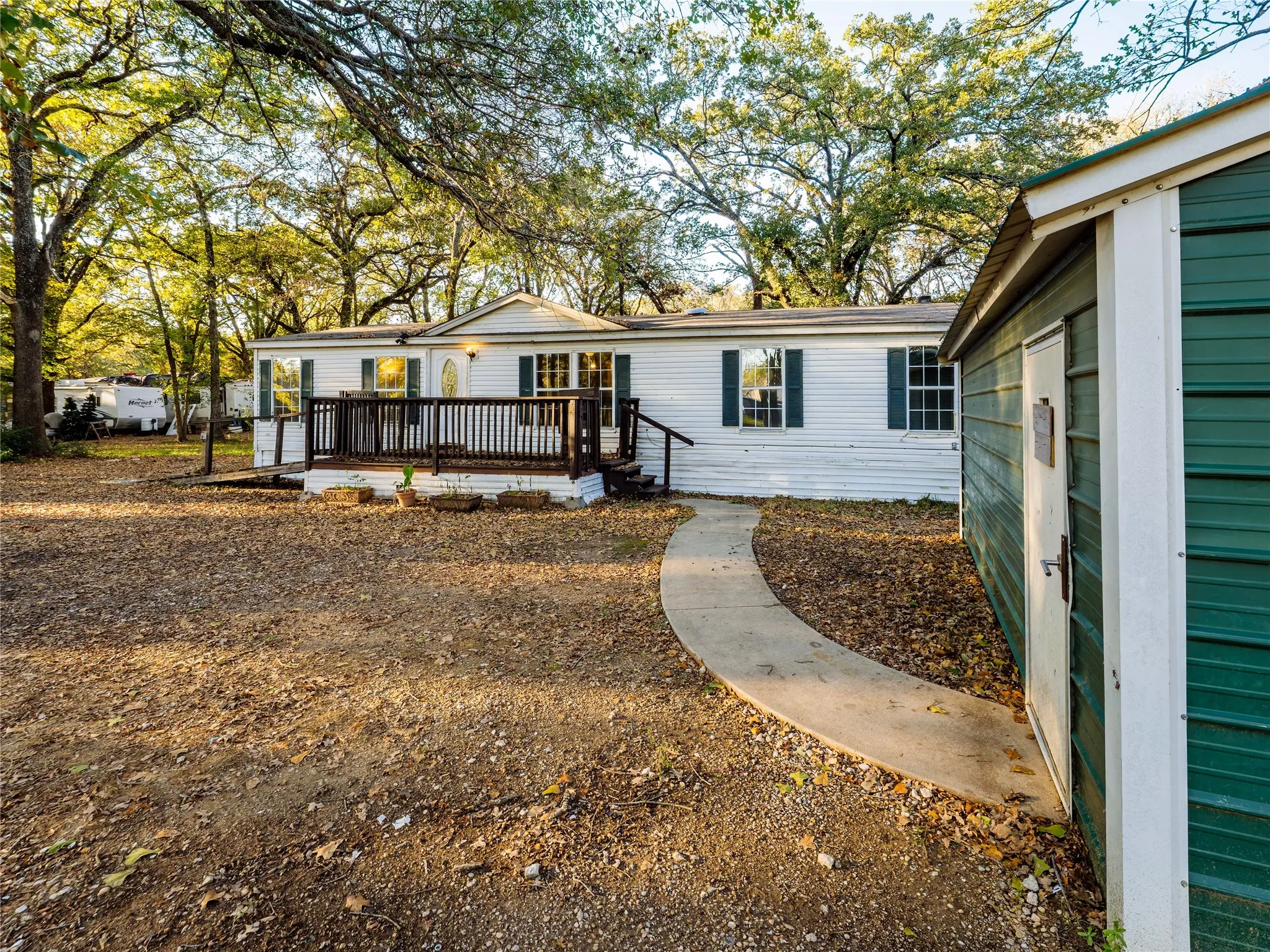 White siding exterior with green window shutters, dark wood deck, and a curved concrete pathway