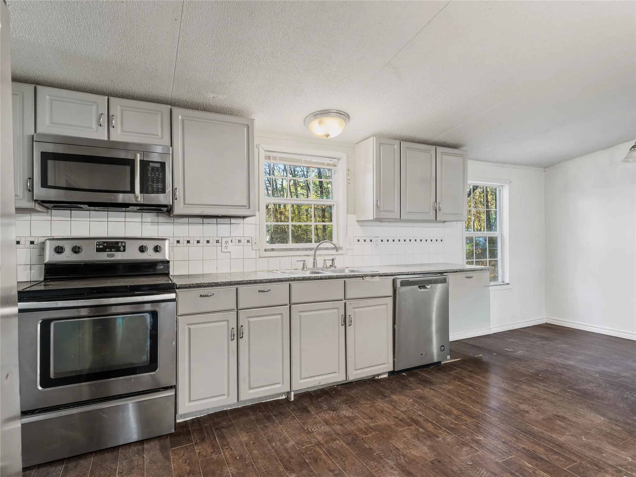 Kitchen featuring stainless steel appliances, wood-finish flooring, white cabinetry, a tiled backsplash, and recessed lighting
