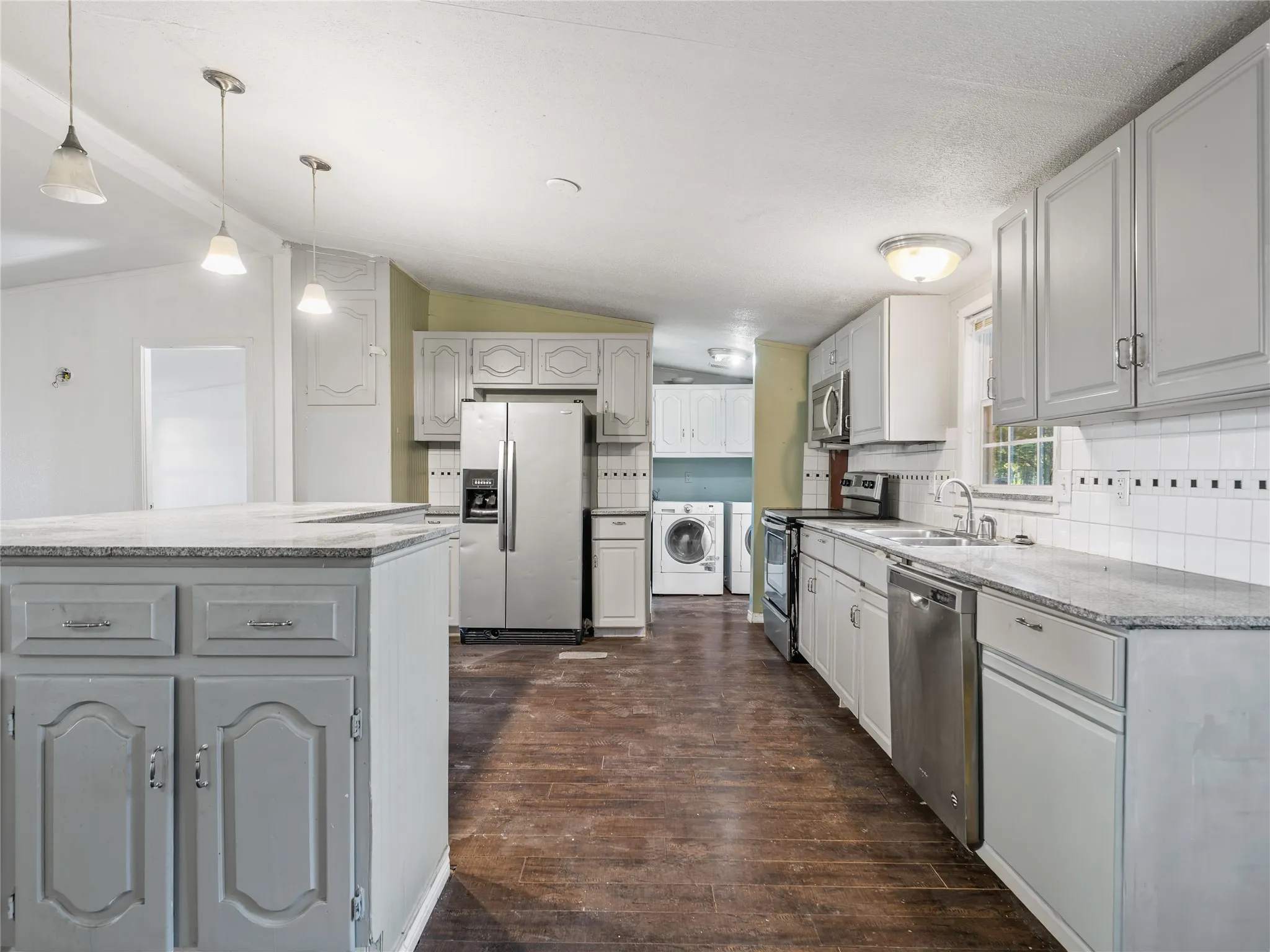 Kitchen featuring an island with a light-toned countertop, gray cabinetry, stainless steel appliances, and wood-finish flooring