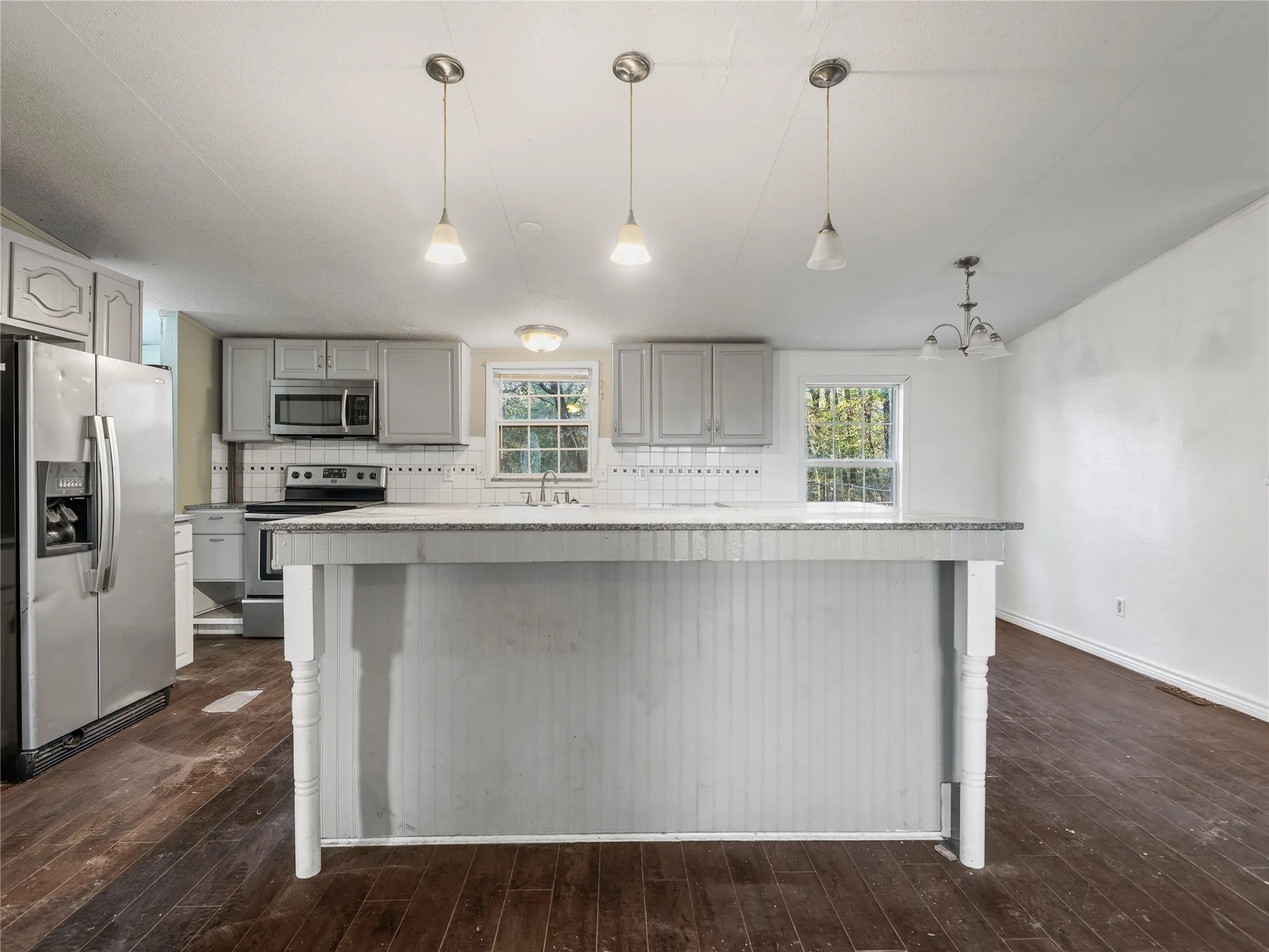 Kitchen featuring gray cabinetry, stainless steel appliances, white tile backsplash, a center island with beadboard detailing, and dark wood-finish flooring