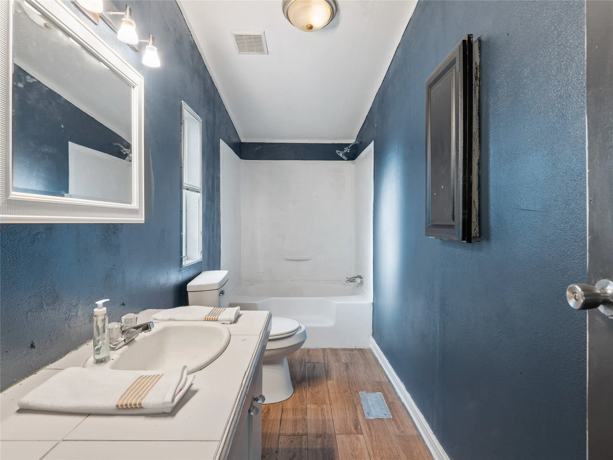 Bathroom featuring a single vanity, wood-finish flooring, and a shower-tub combination