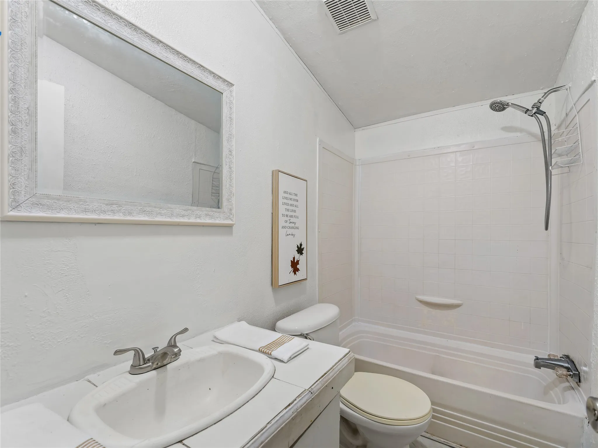 Clean and functional bathroom featuring a white porcelain sink with brushed nickel faucet, framed mirror with white finish, white subway tile walls, and an integrated shower-tub combination with chrome fixtures and glass enclosure panel