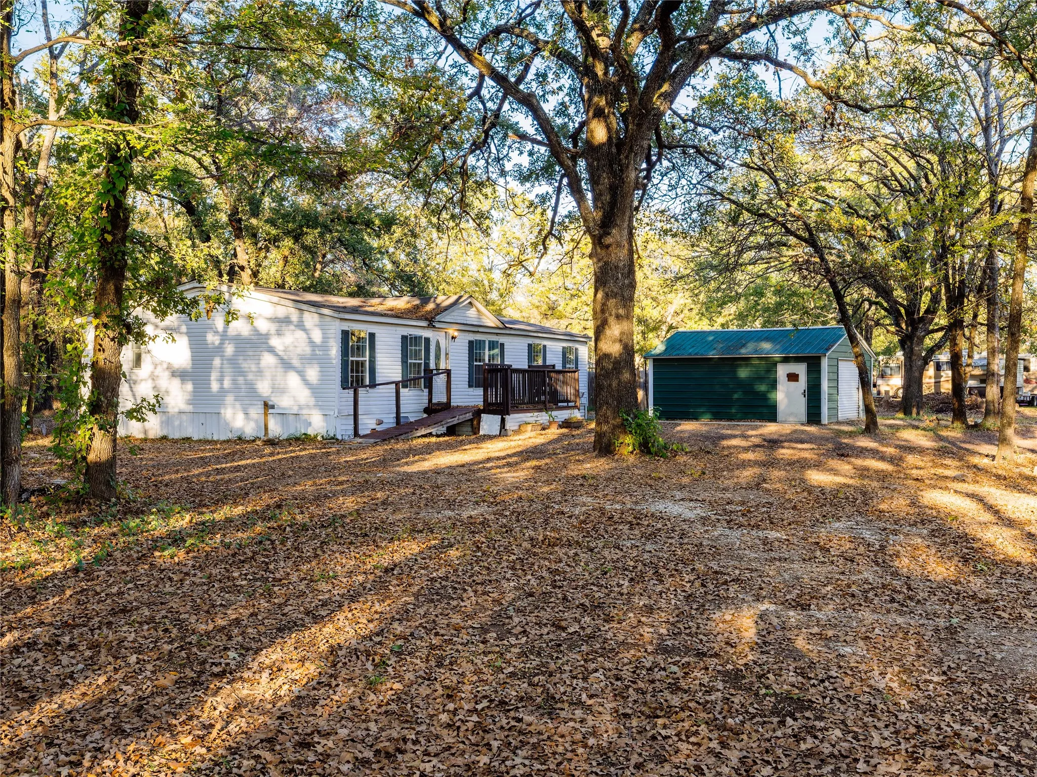 White exterior residence with dark shutters, front porch with ramp access, mature trees, and a detached shed with a green metal roof