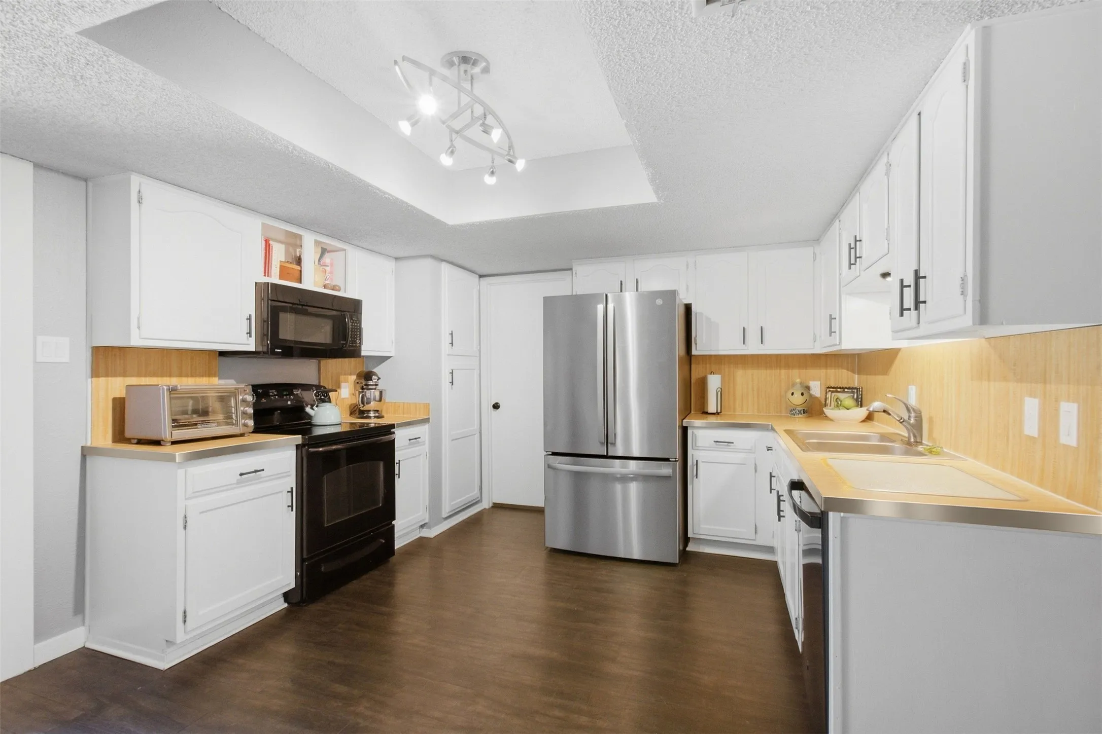 White cabinetry with black hardware, stainless steel appliances, wood-finish flooring, and a unique track lighting fixture