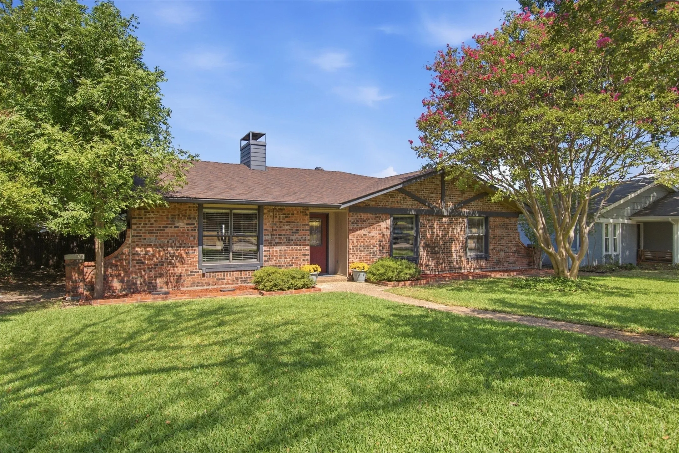 Brick exterior with a brown shingle roof, a red front door, and established trees framing the property