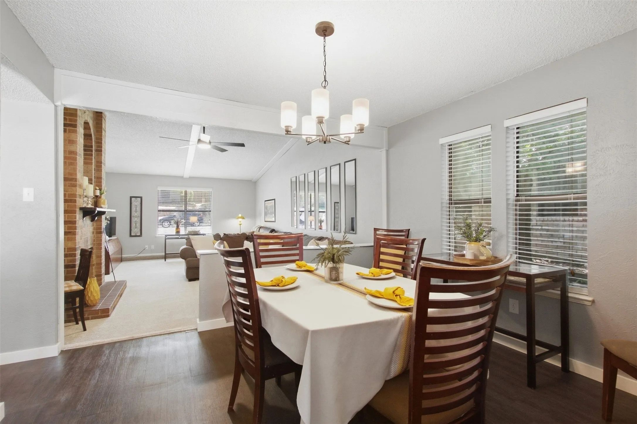 Hardwood-finish flooring, contemporary chandelier, multiple windows with blinds, brick fireplace surround, vaulted ceiling