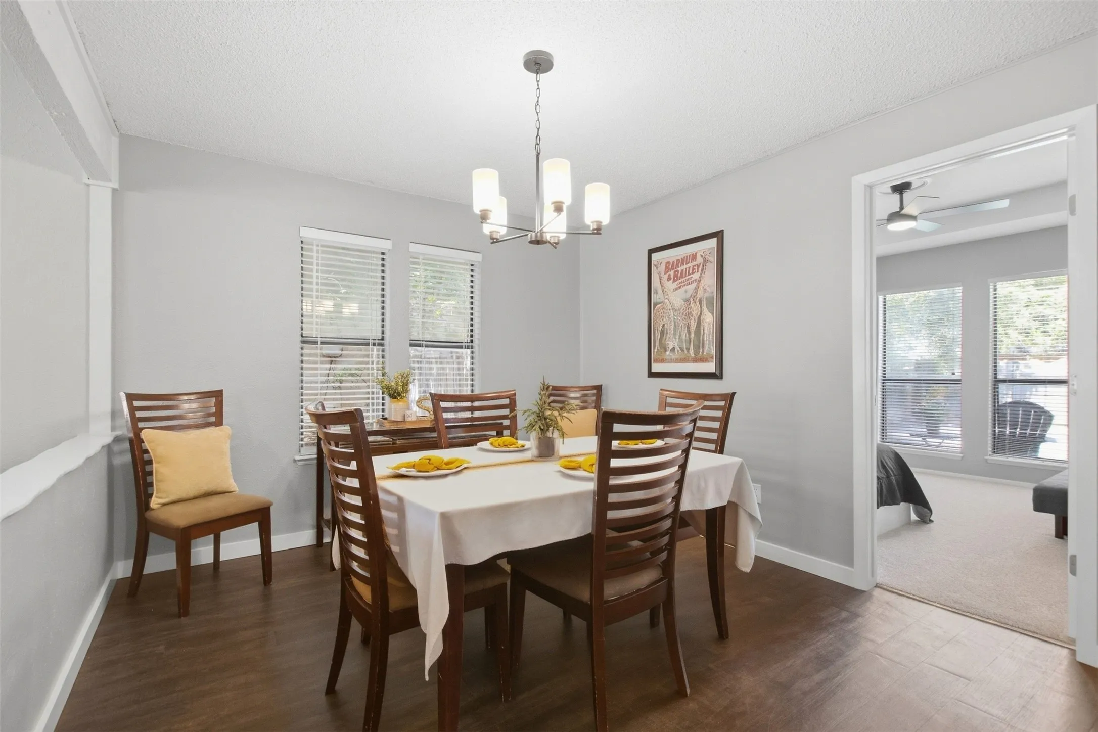 Dining area featuring wood-finish flooring, two large windows with blinds, and a multi-light chandelier