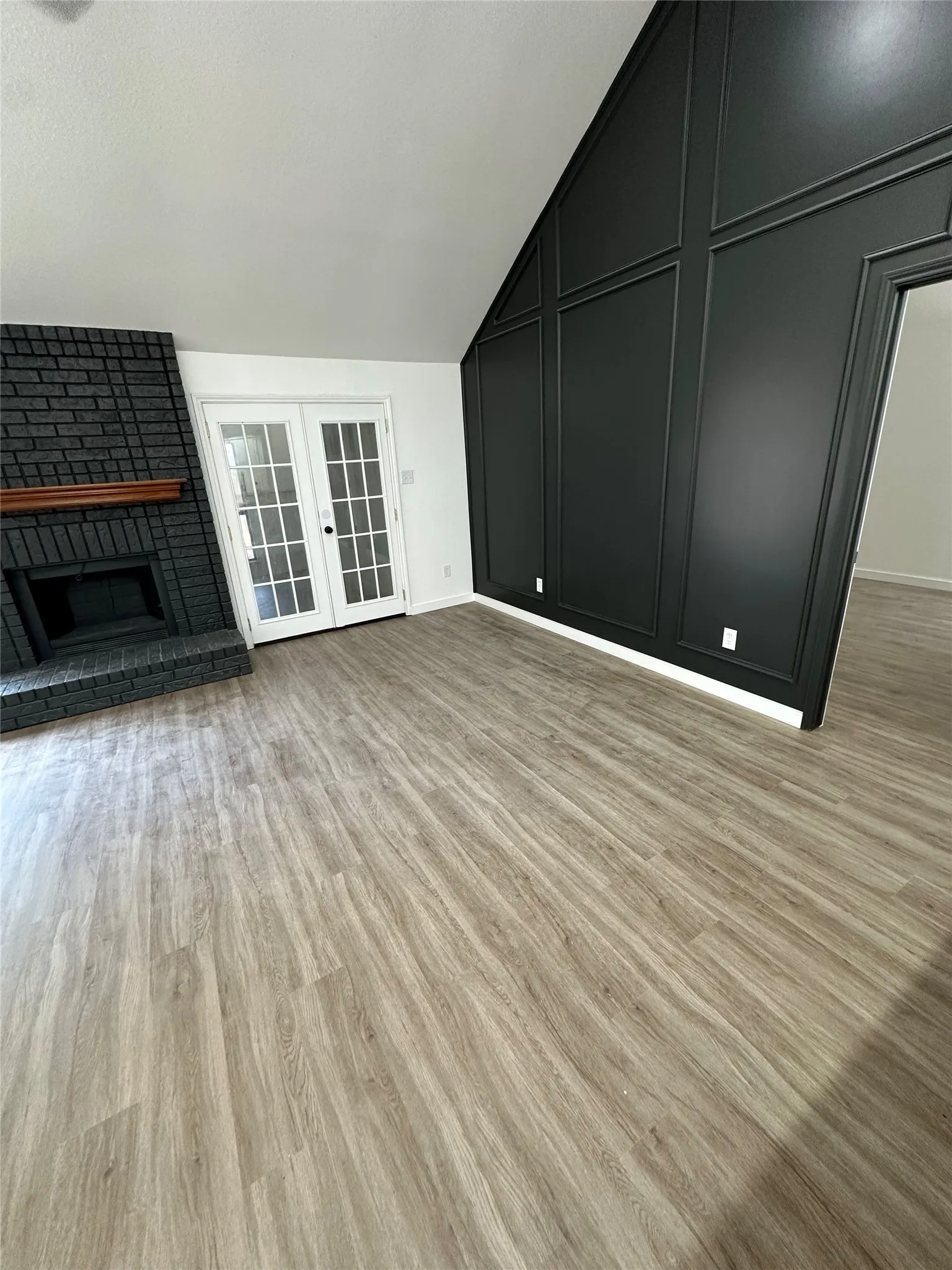 Wood-finish flooring throughout, complemented by a black brick fireplace with a wood mantle, and white French doors
