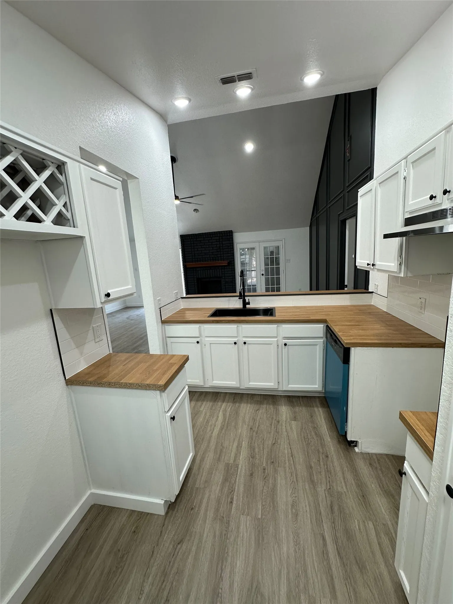 Kitchen featuring wood-finish countertops, white cabinetry with black hardware, and a black undermount sink
