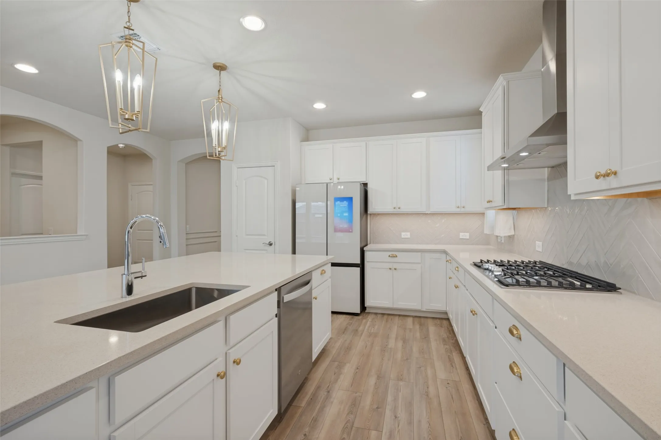 Kitchen featuring white cabinetry, light-toned countertops, a stainless steel gas cooktop, a built-in stainless steel dishwasher, and wood-finish flooring