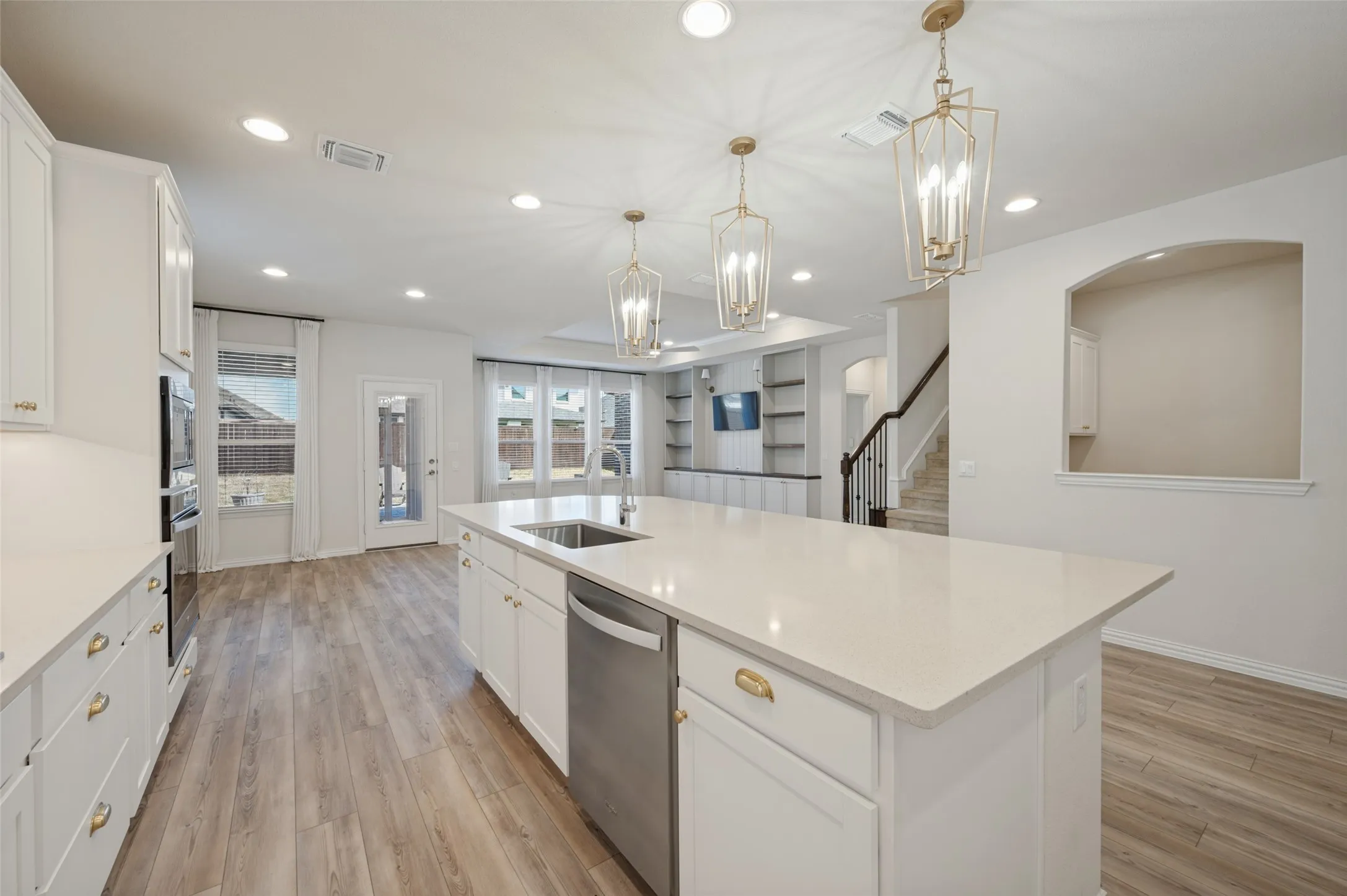 Spacious kitchen featuring an expansive island with a stainless steel sink, white cabinetry with brass hardware, and wood-finish flooring
