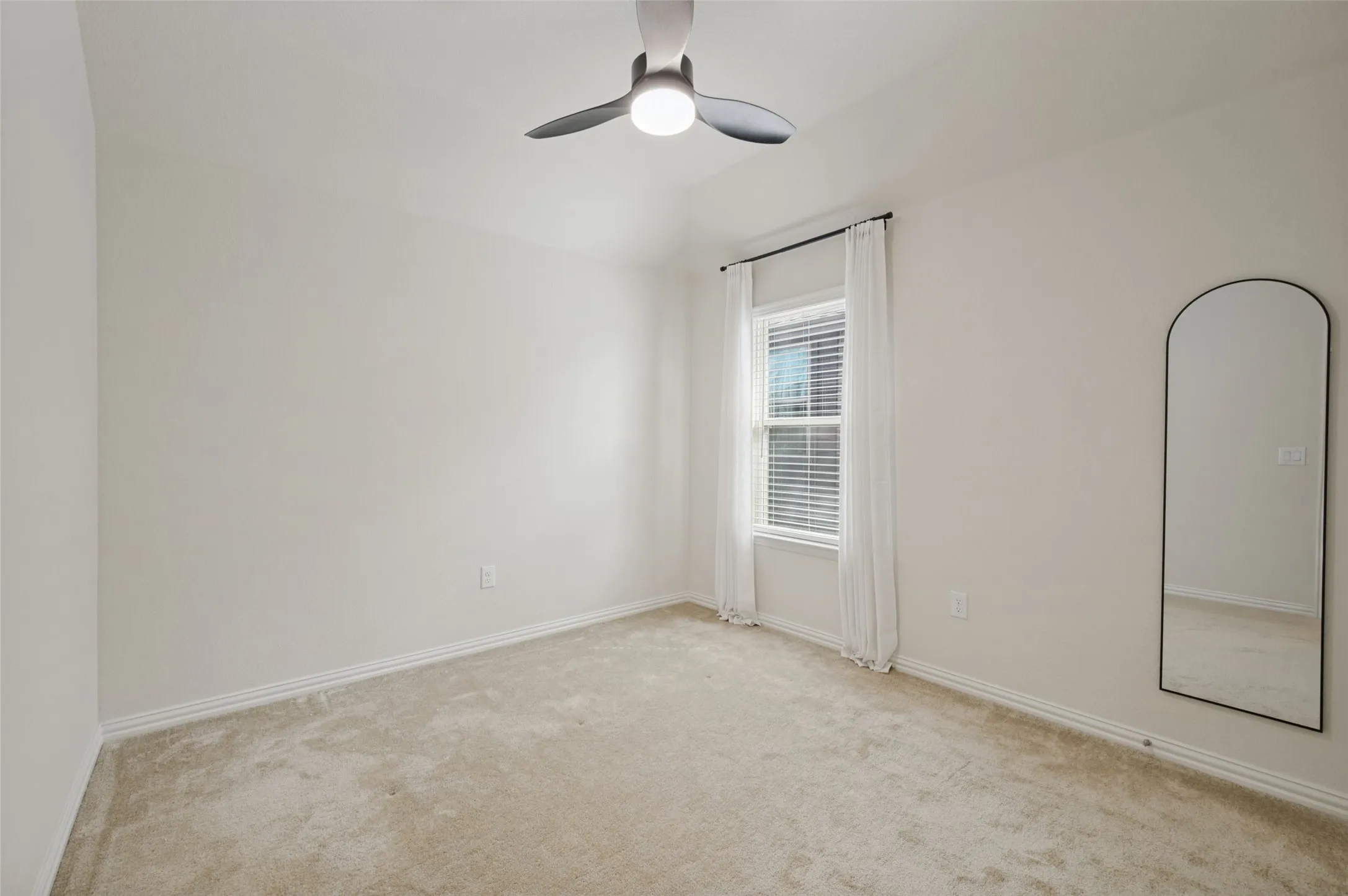 Neutral wall color and carpeting, featuring a window with blinds, and a ceiling fan with integrated lighting