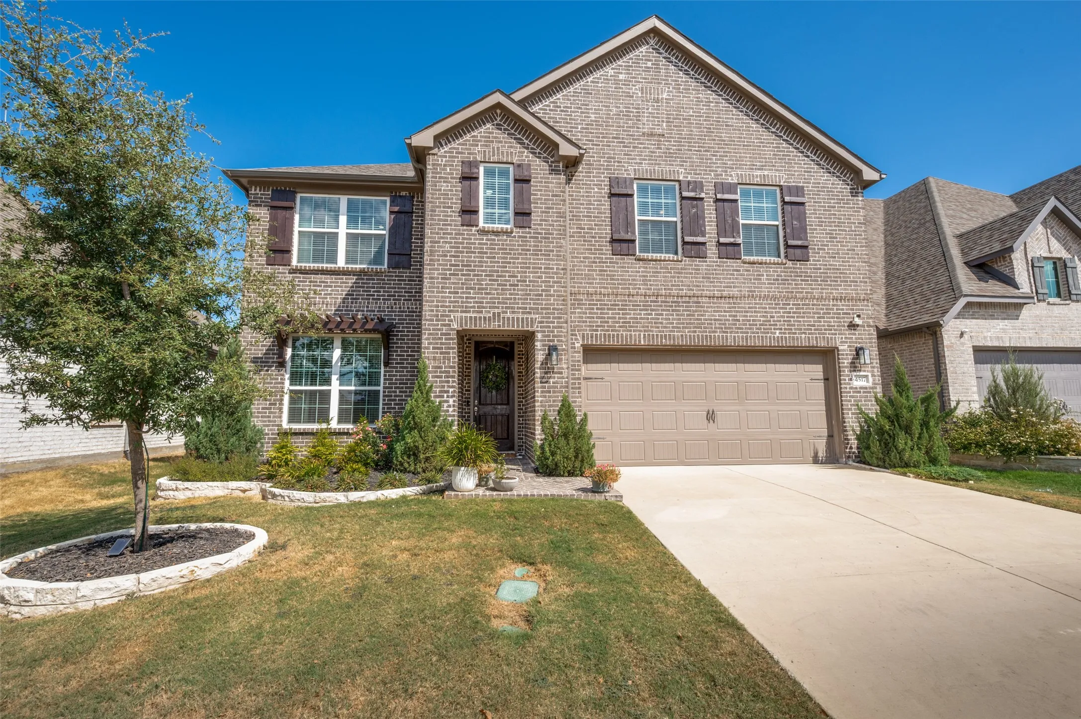 Two-story brick exterior with shutters, an attached two-car garage, concrete driveway, and front landscaping