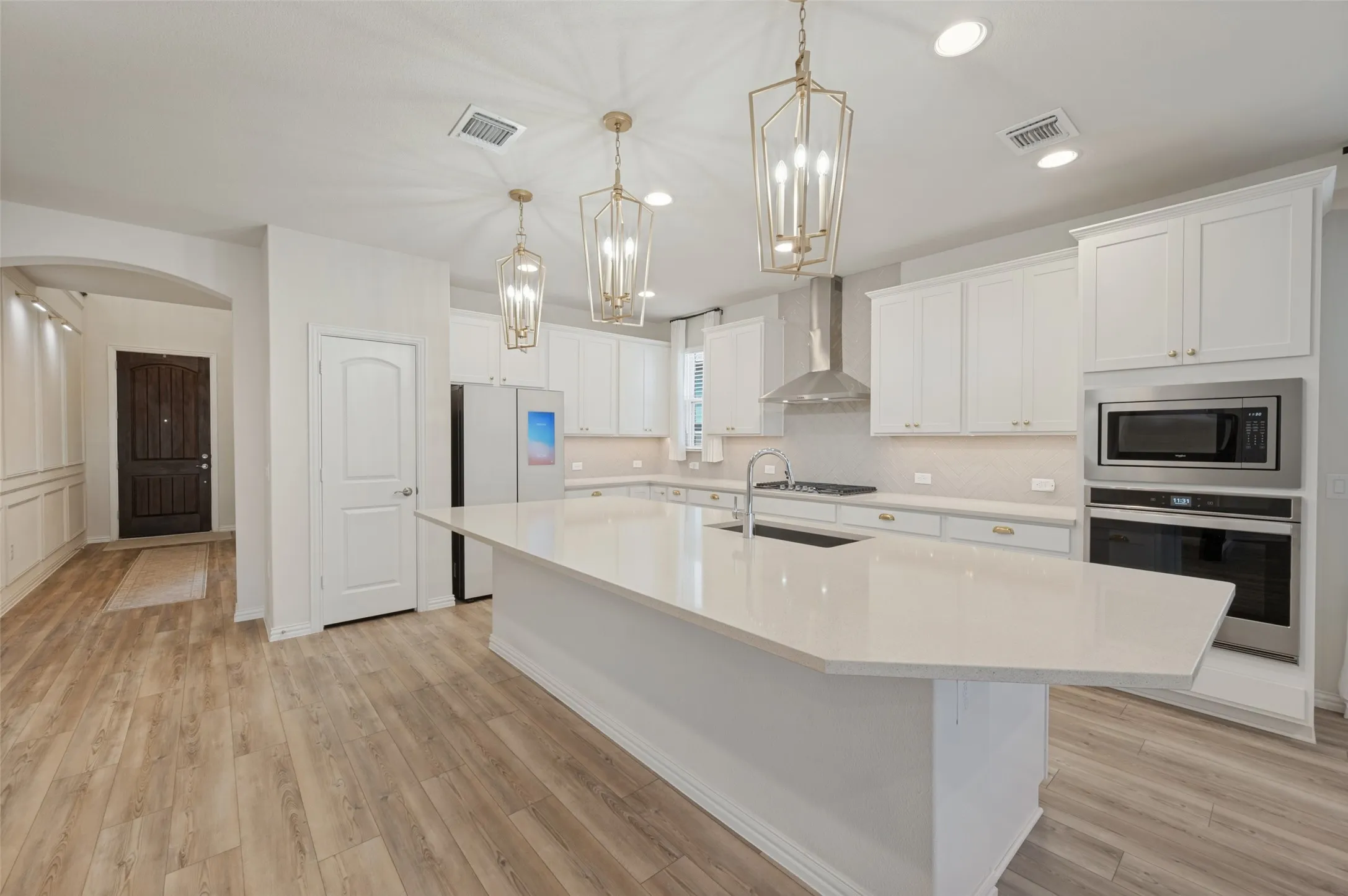 Spacious kitchen featuring an expansive island, white cabinetry, integrated stainless steel appliances, and wood-finish flooring