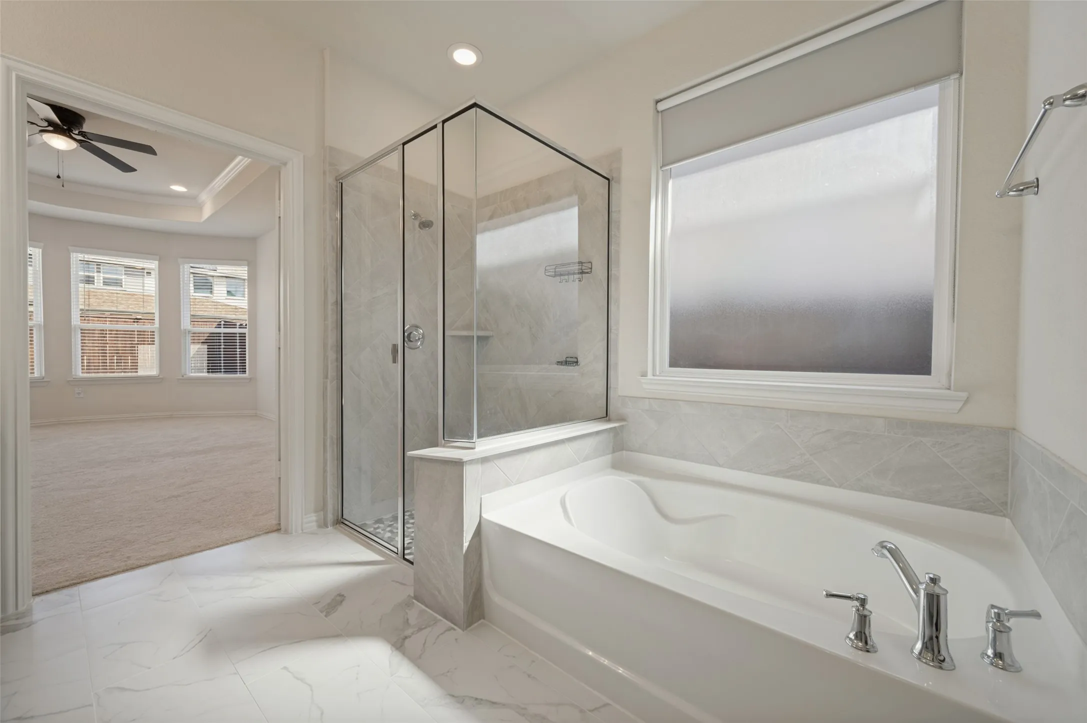 Freestanding soaking tub with chrome fixtures, glass-enclosed shower with tile surround, recessed lighting, and large window with roller shade