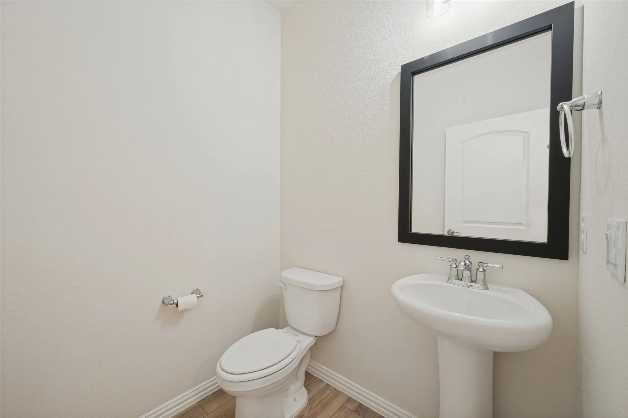 Pedestal sink with chrome faucet, framed mirror, and wood-finish flooring
