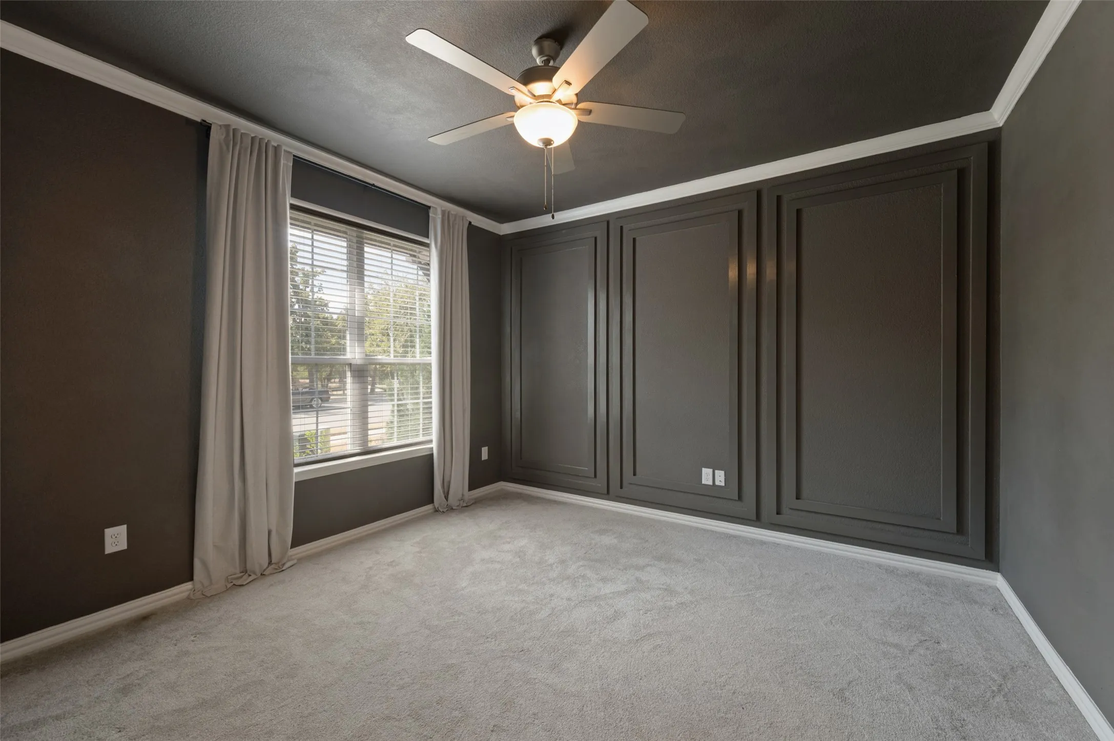 Recessed panel wall detailing, crown molding, ceiling fan with integrated lighting, window with blinds, and light gray carpeting