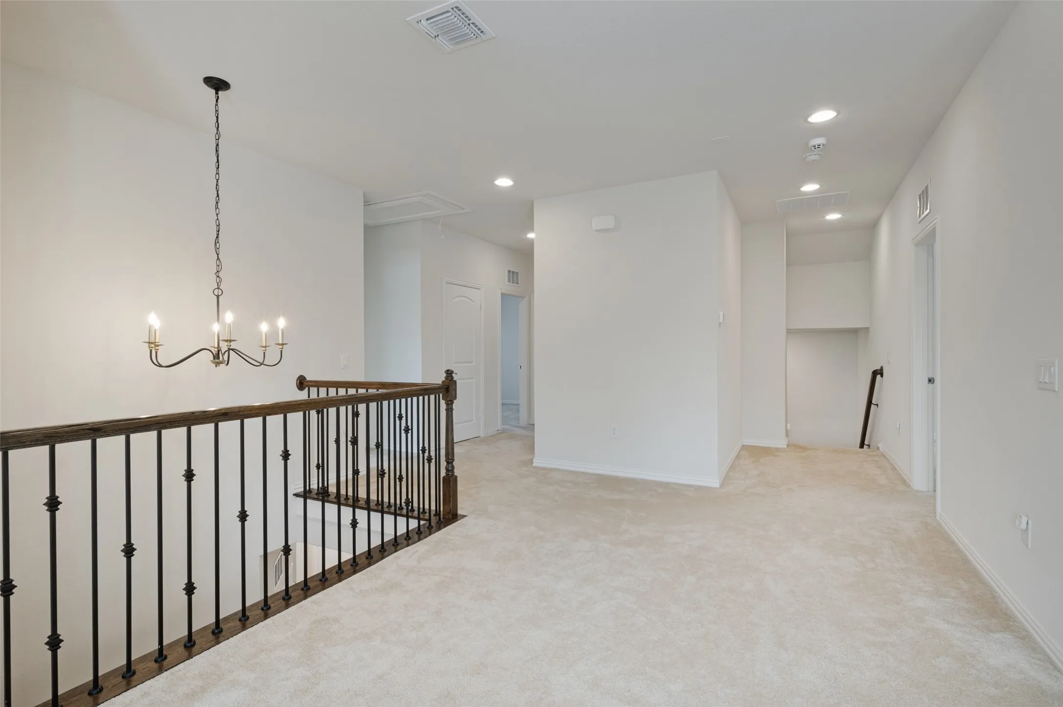 Plush carpeting, recessed lighting, and a wrought iron chandelier illuminate this spacious landing