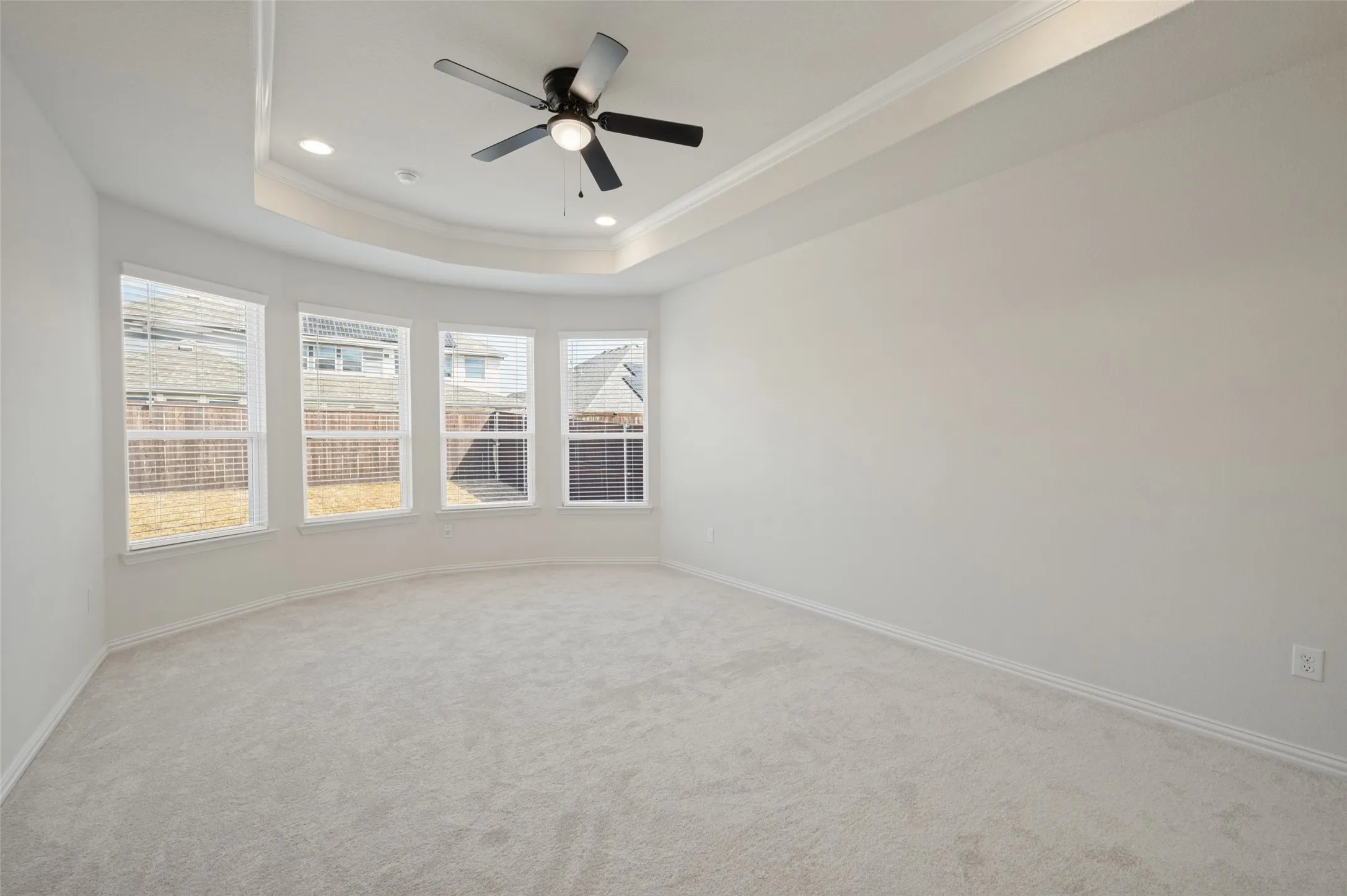 Tray ceiling with recessed lighting and a ceiling fan, bay window with four individual windows, light-toned carpeting
