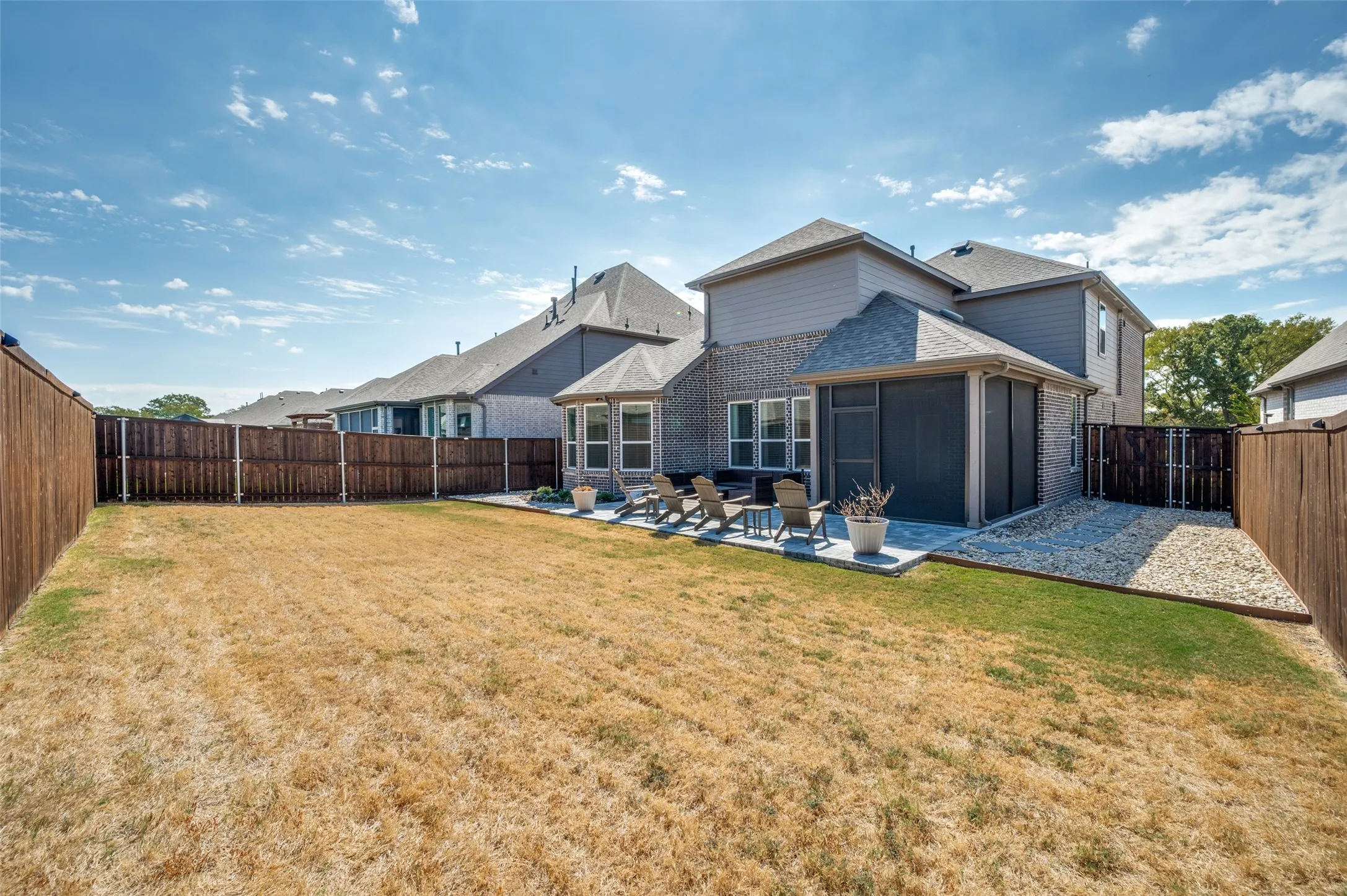 Backyard featuring a paved patio area, screened enclosure, and a gravel hardscaping section