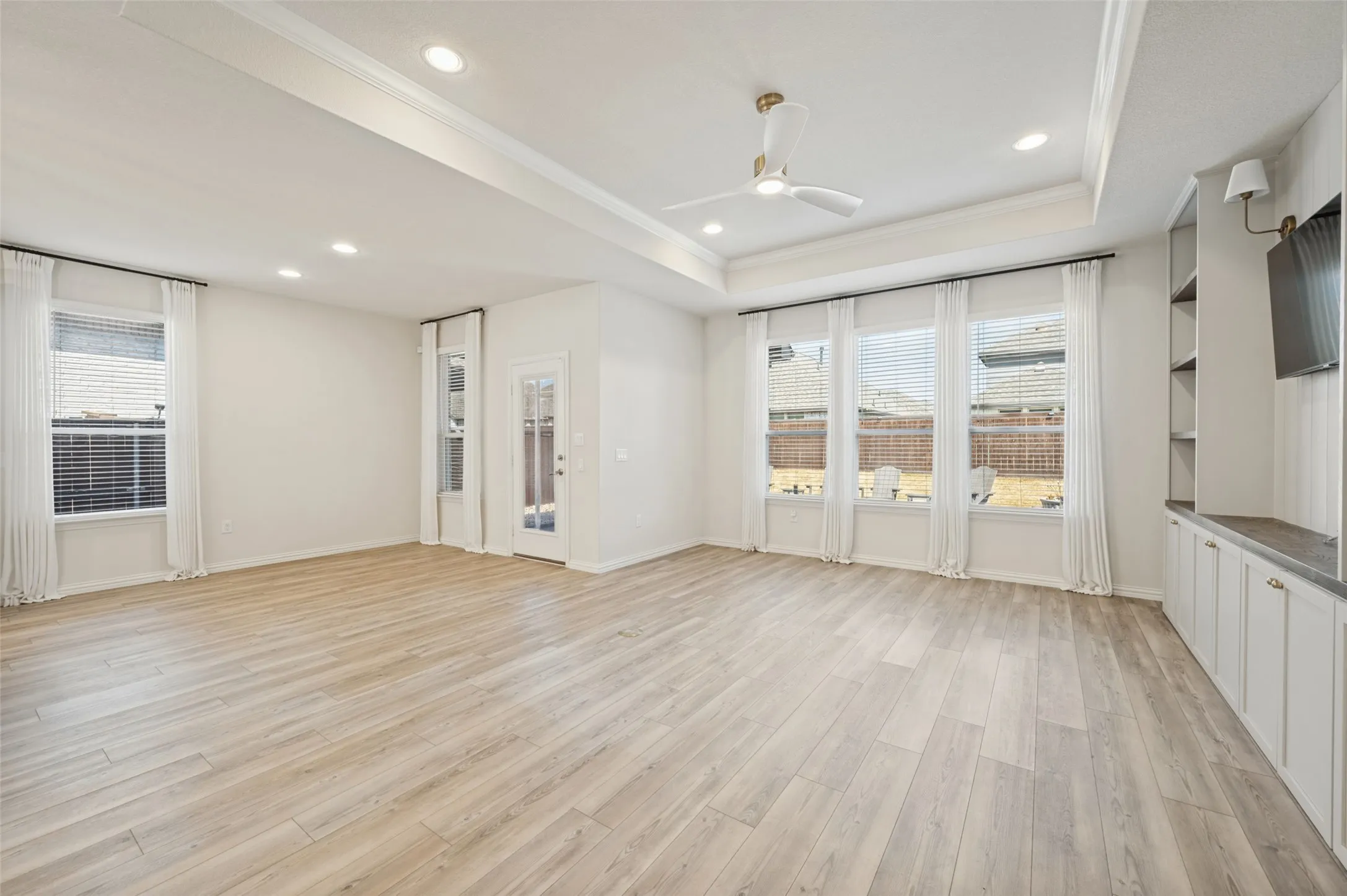 Tray ceiling with recessed lighting and a ceiling fan, wood-finish flooring, built-in cabinetry with open shelving, and multiple windows