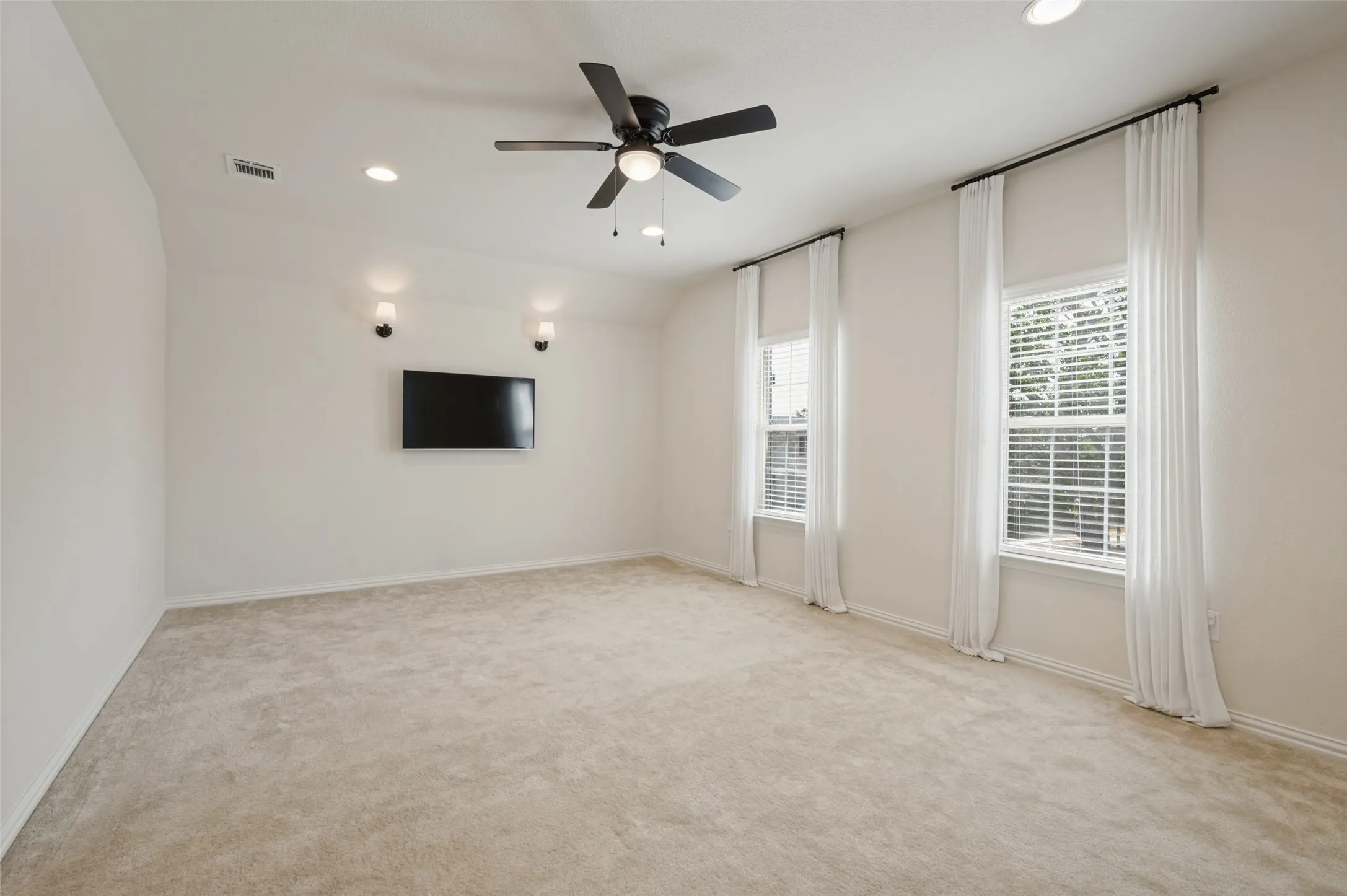 Recessed lighting, ceiling fan, sconce lighting, two windows with blinds, and carpeted flooring