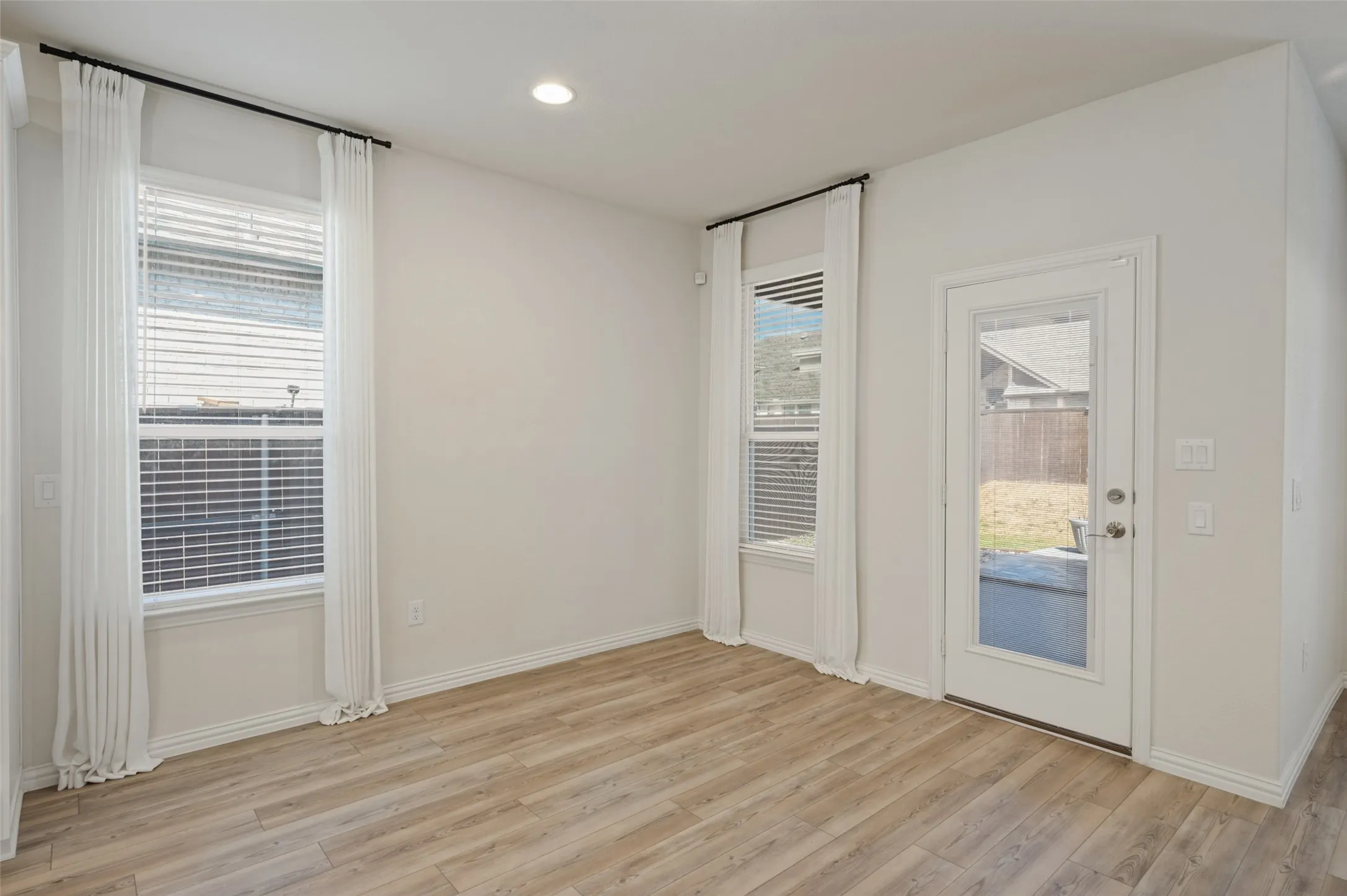 Spacious room featuring wood-finish flooring, recessed lighting, and ample natural light from multiple windows and a glass-paneled door