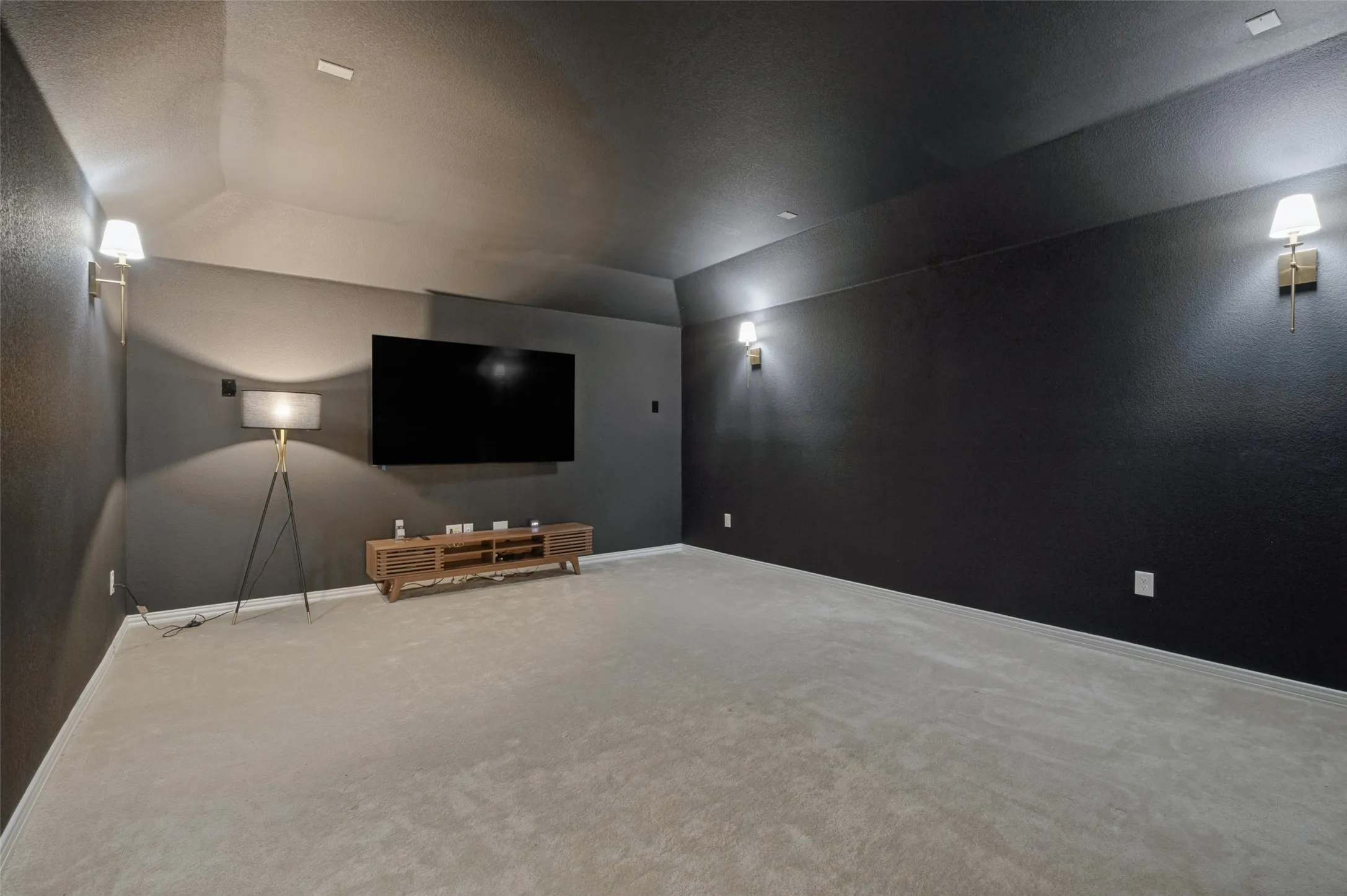 Spacious room featuring carpeting, dark wall finishes, sloped ceiling, and multiple wall-mounted sconces