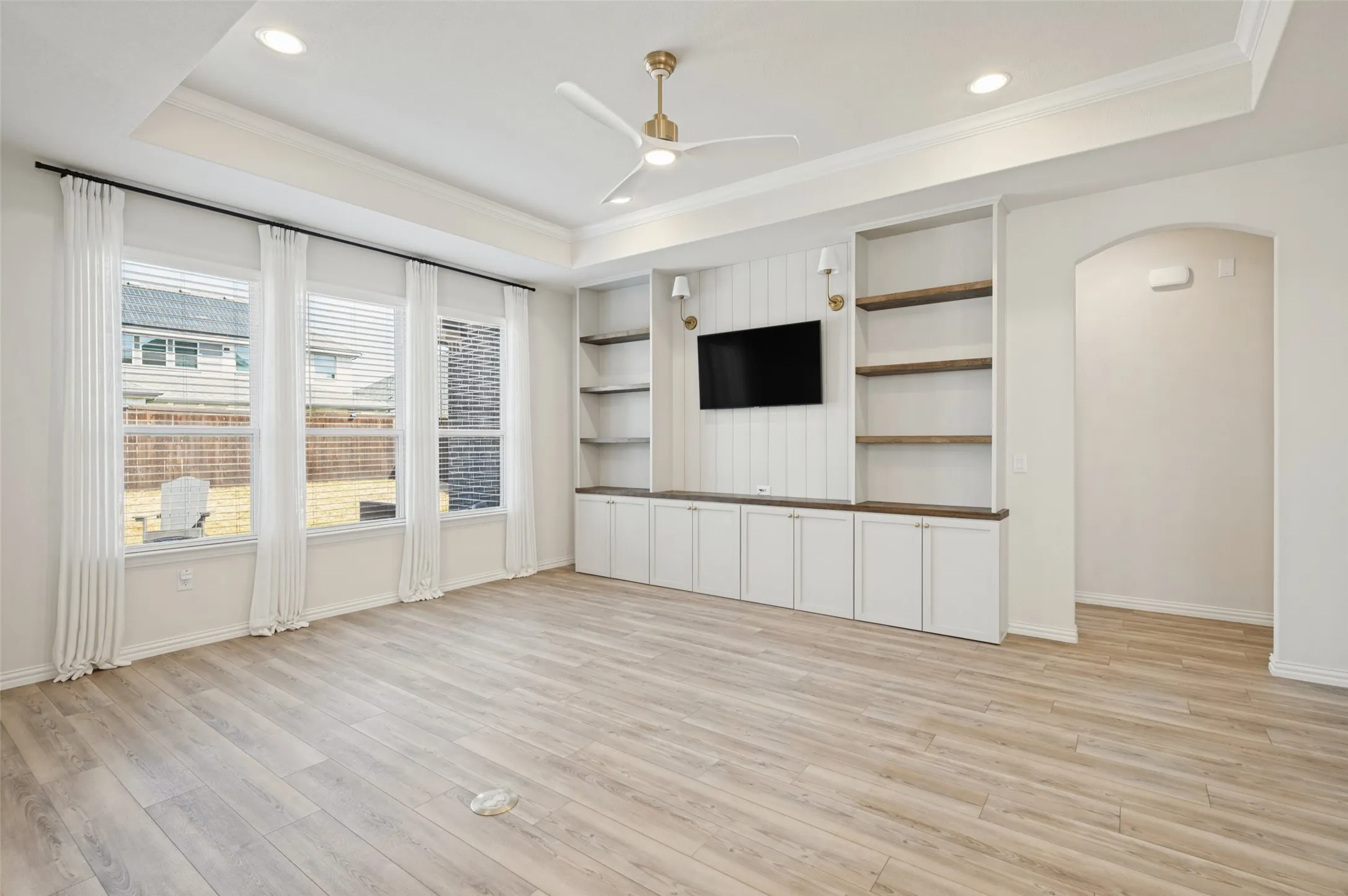 Tray ceiling with recessed lighting, wood-finish flooring, built-in cabinetry with wood-finish countertops, built-in shelving, and multiple windows