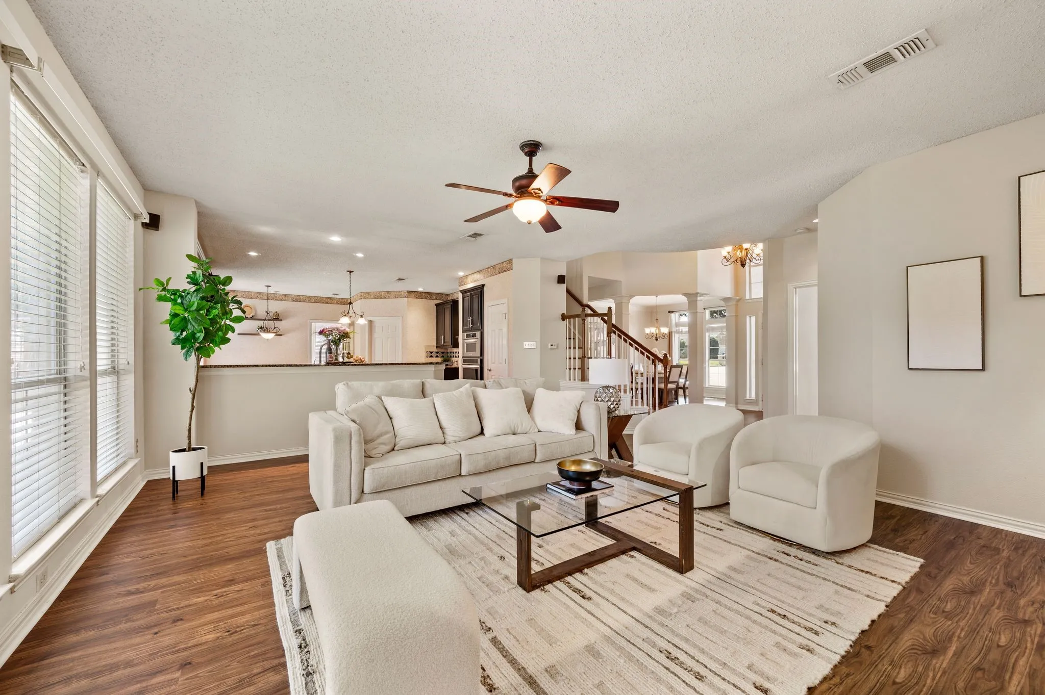 Open-concept living area featuring wood-finish flooring, a ceiling fan, and large windows with blinds