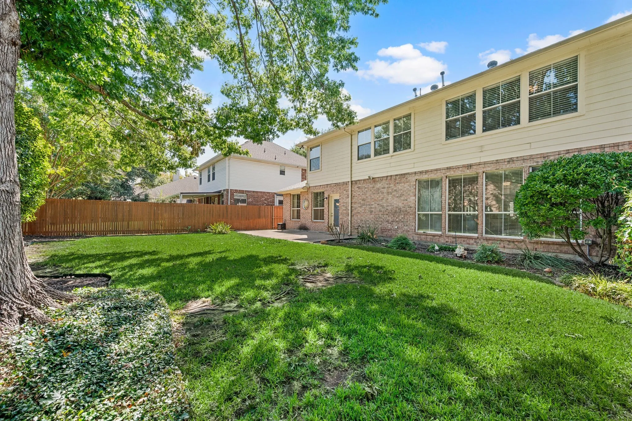Expansive backyard featuring a manicured lawn, established shade trees, and a privacy fence