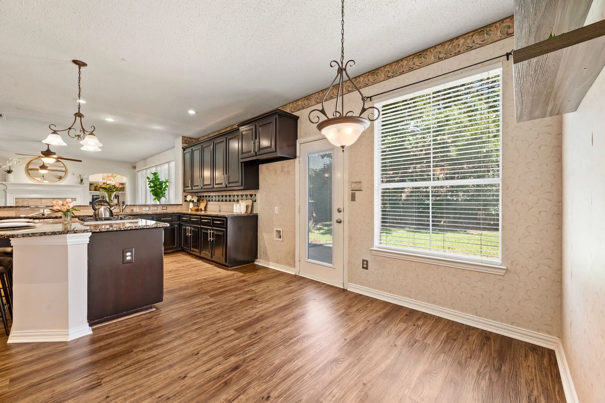 Wood-finish flooring throughout, dark wood cabinetry, and a kitchen island with stone countertop