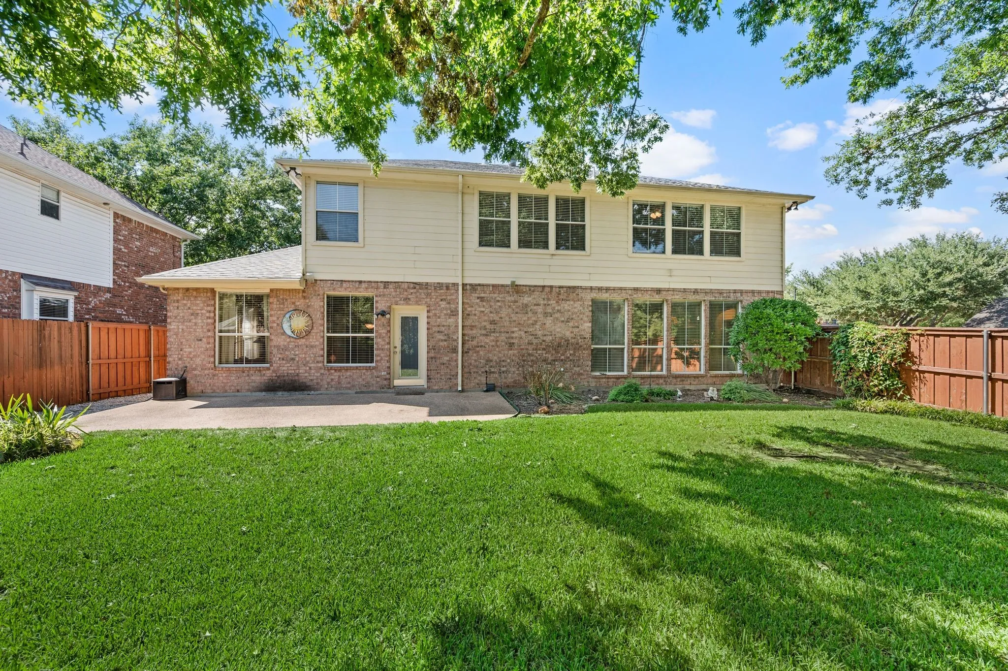 Expansive backyard featuring a manicured lawn, concrete patio, brick and siding exterior, and a privacy fence