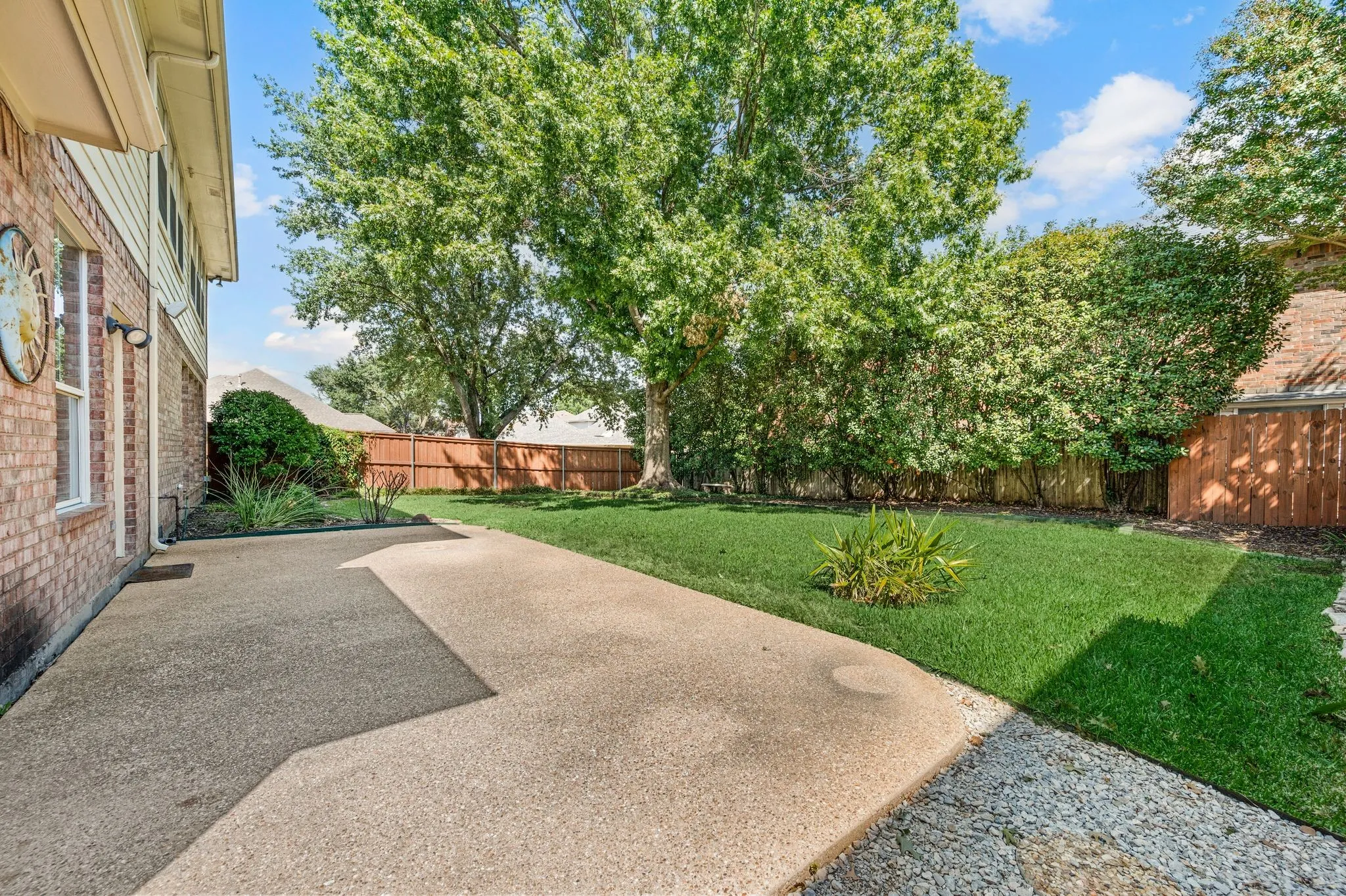Expansive backyard featuring a manicured lawn, established mature trees, and a concrete patio